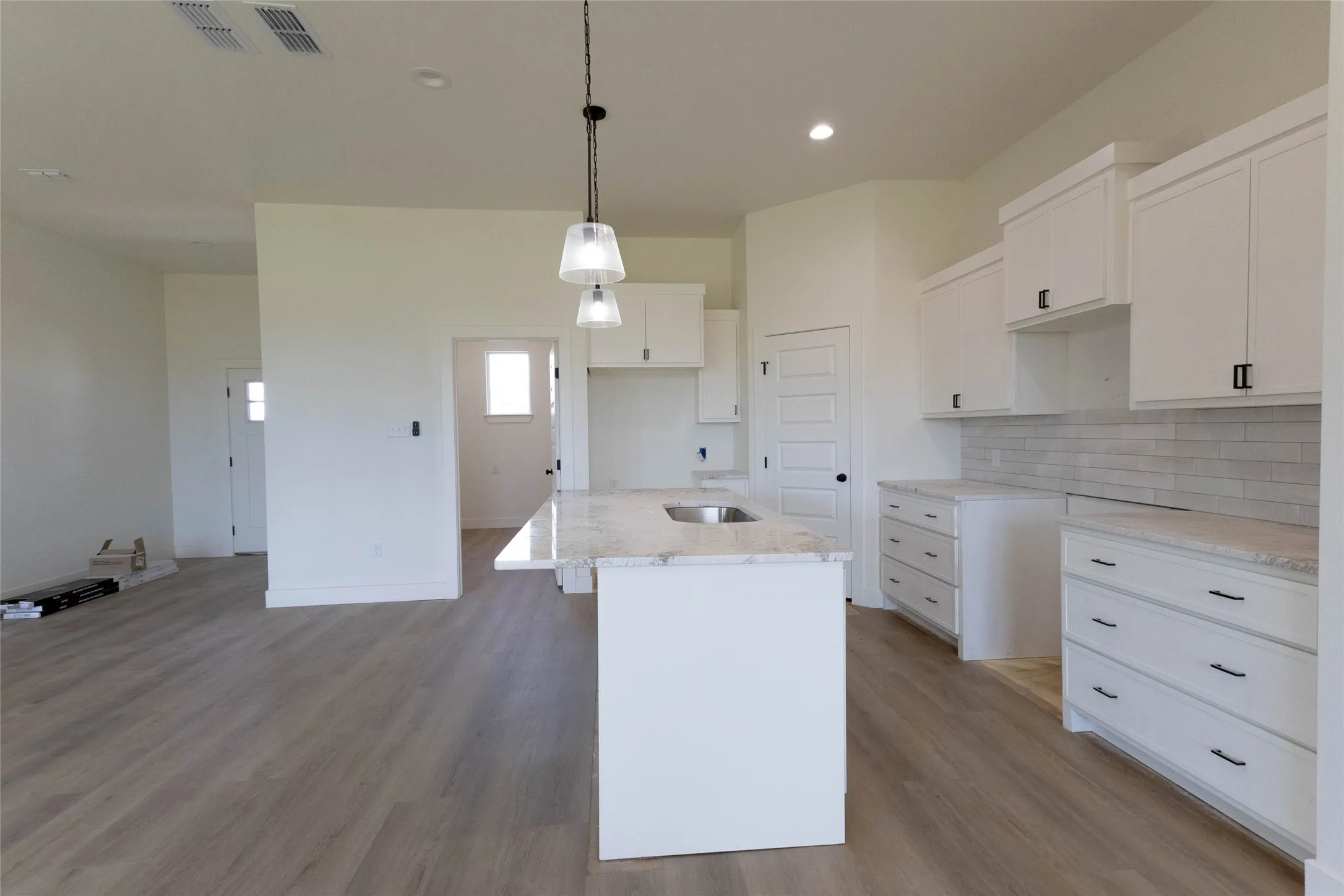 Spacious kitchen featuring white cabinetry with dark hardware, a center island with an undermount sink, light-toned countertops, and a subway tile backsplash