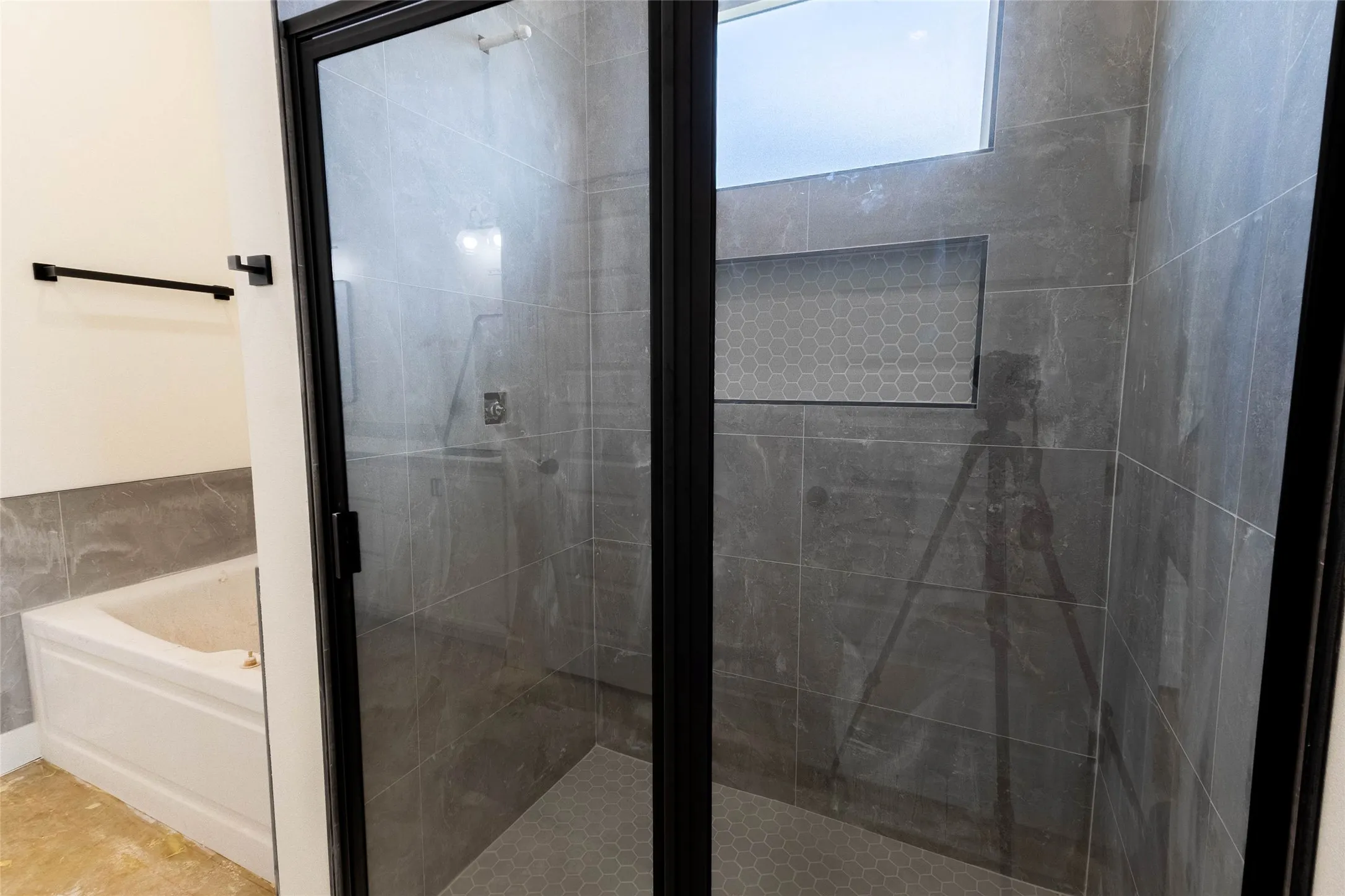 Walk-in shower with dark-framed glass enclosure, grey large-format tile walls, and a hexagonal mosaic tile floor