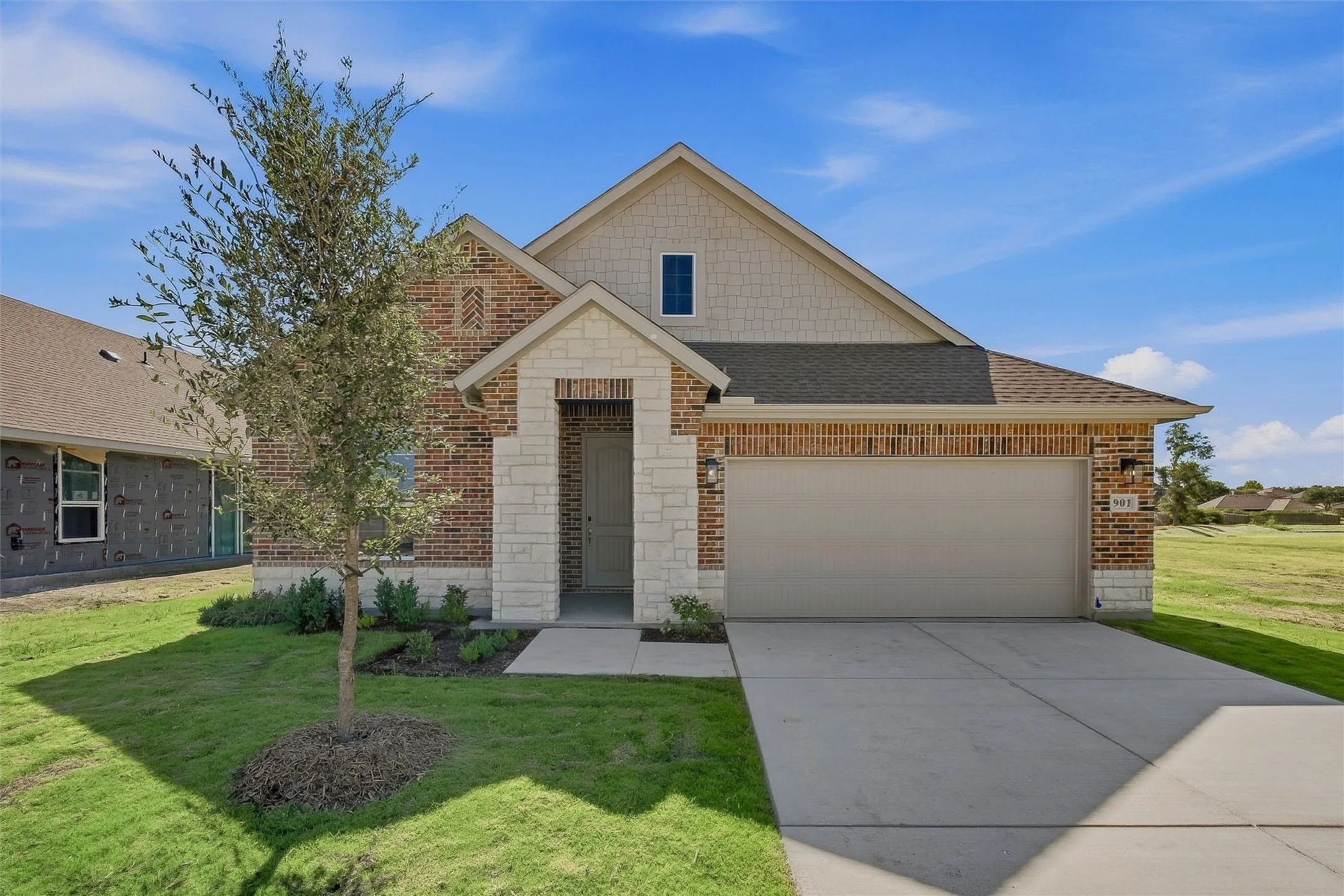 Brick and stone exterior with a covered entry, attached two-car garage, and concrete driveway