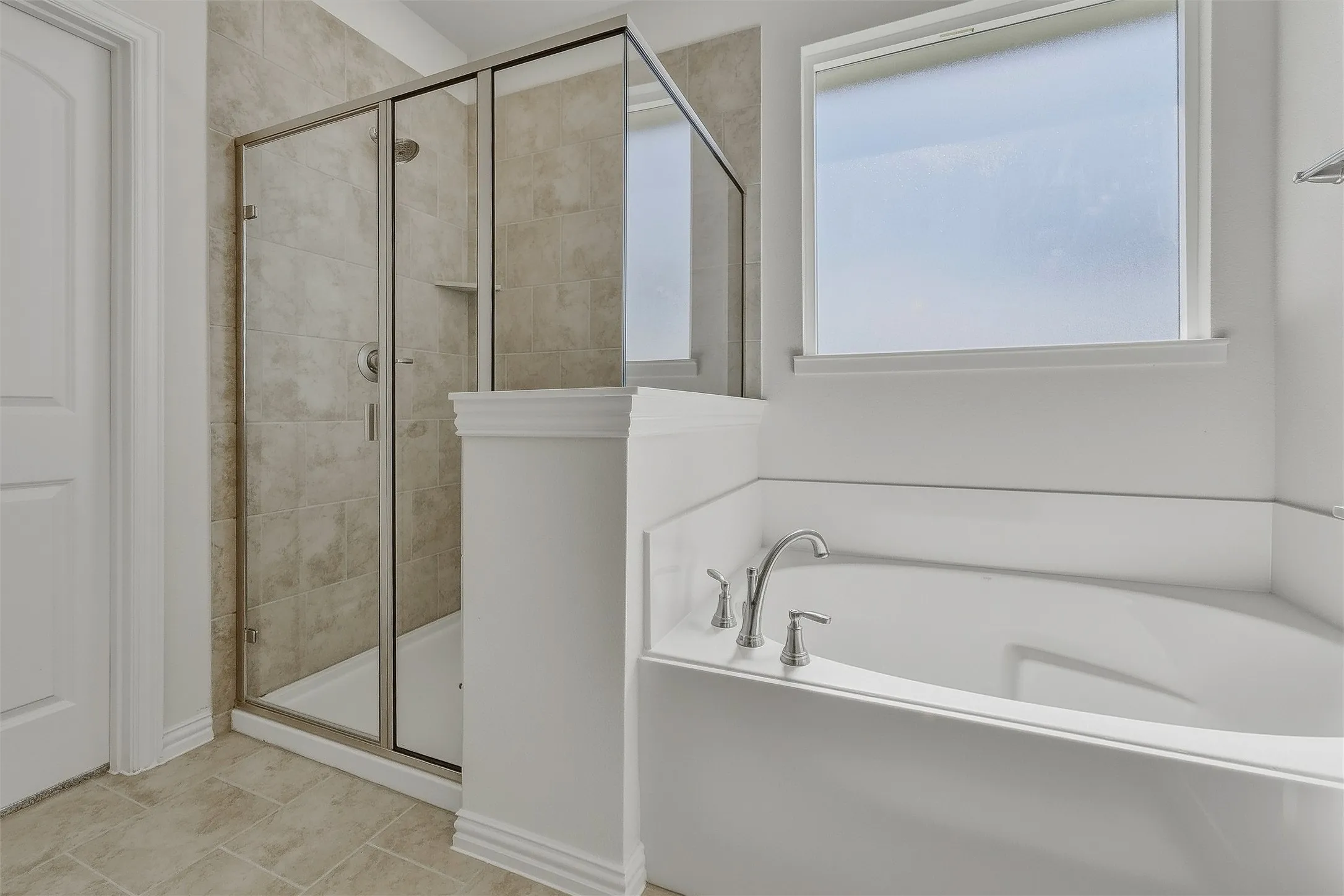 Built-in soaking tub with chrome fixtures, enclosed shower with floor-to-ceiling tile, and a frosted window