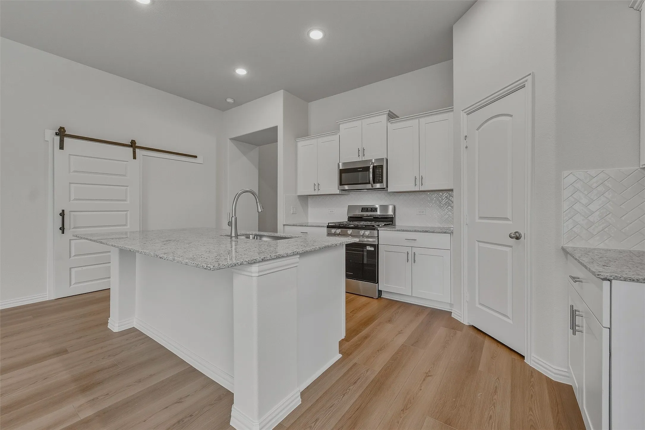 Kitchen featuring wood-finish flooring, recessed lighting, white cabinetry, a kitchen island with a sink, and stainless steel appliances