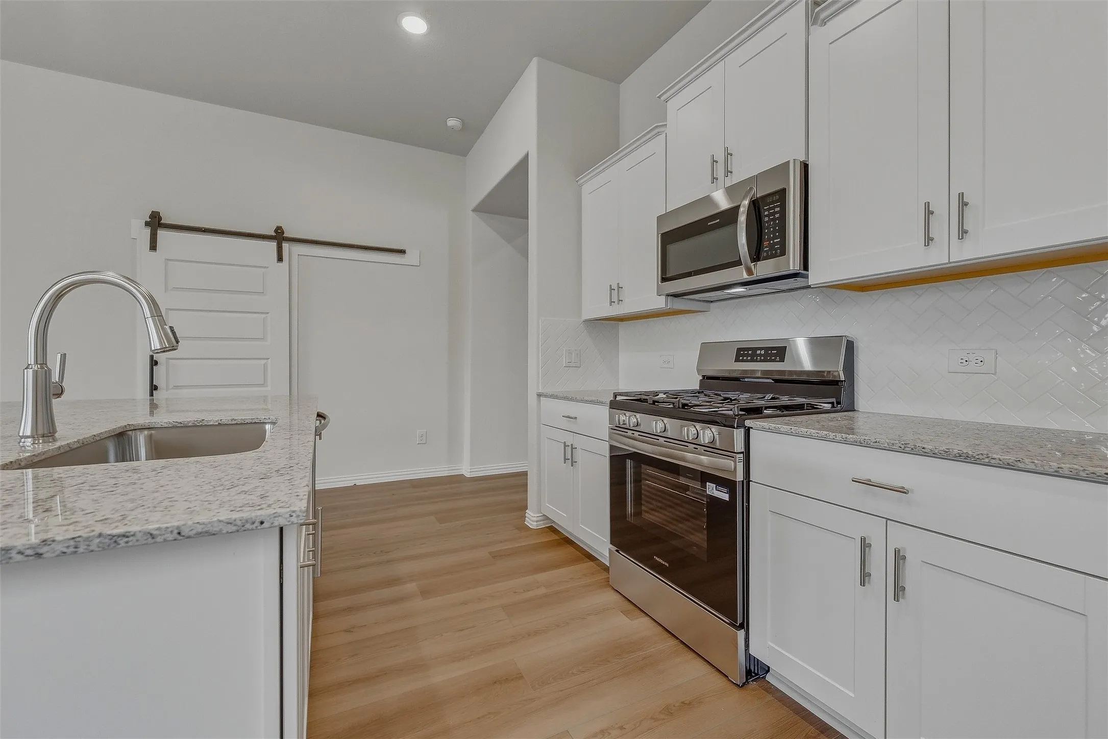White cabinetry, stainless steel appliances, granite countertops, wood-finish flooring, and a barn door entry