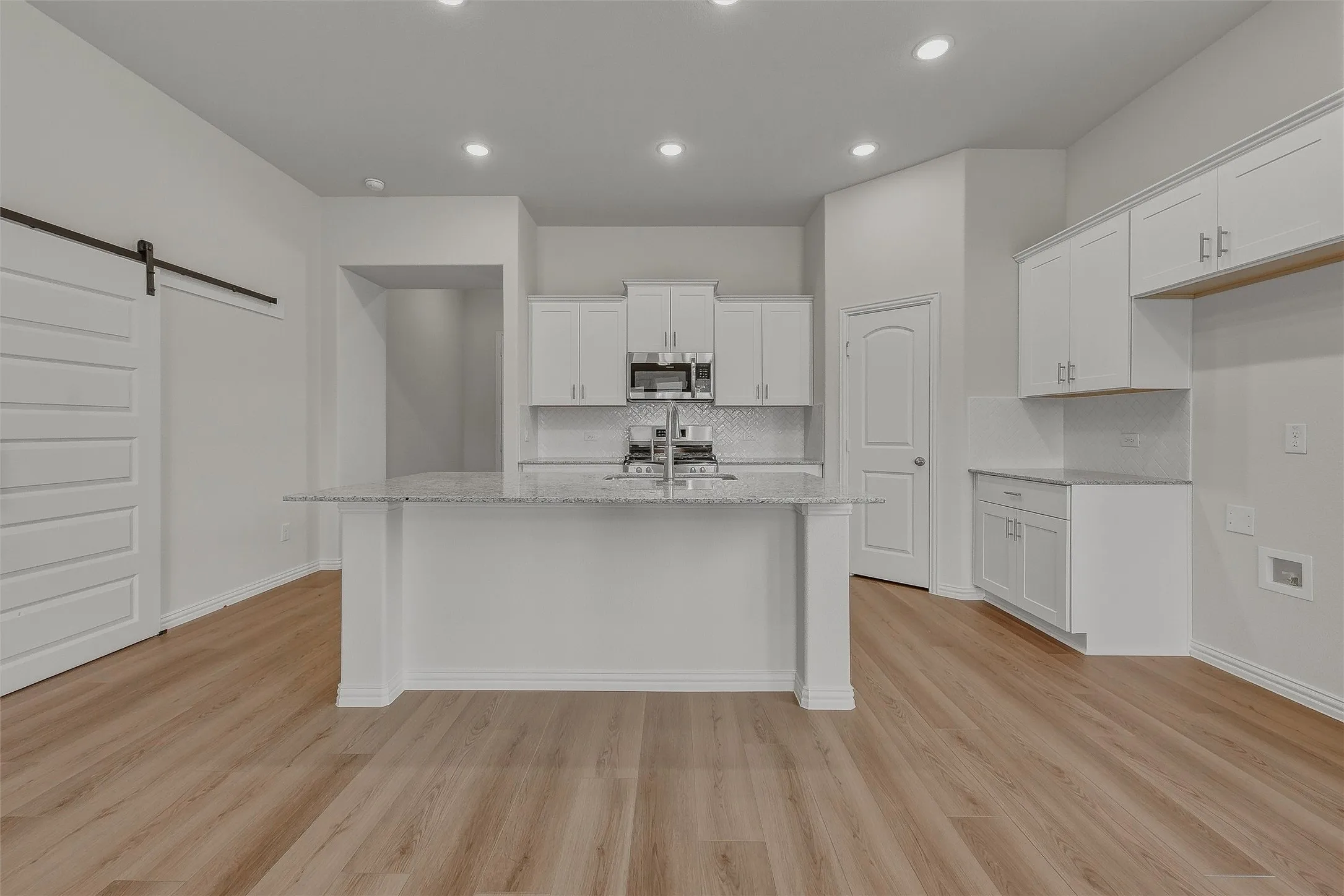 Kitchen featuring a central island with a light-toned countertop, white cabinetry with silver-toned hardware, stainless steel microwave, and wood-finish flooring