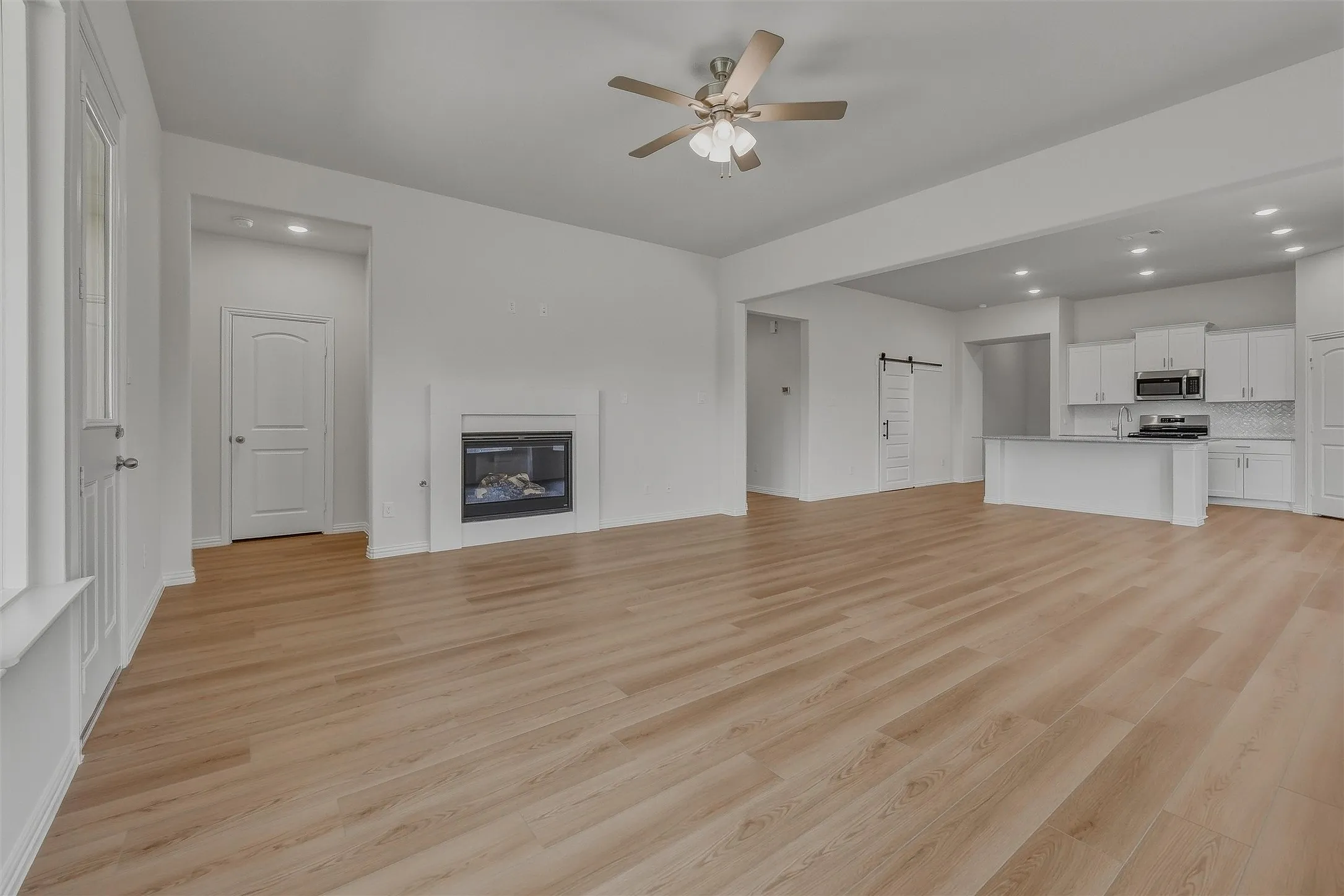 Spacious open-concept living area featuring wood-finish flooring, a contemporary fireplace, and an integrated kitchen with an island