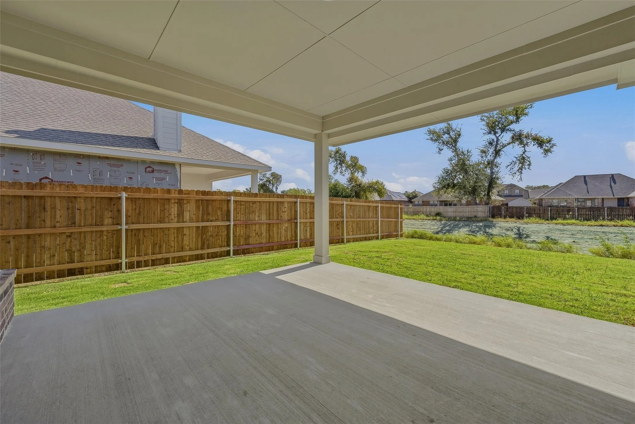 Covered patio with a concrete surface, expansive lawn, and wood privacy fencing