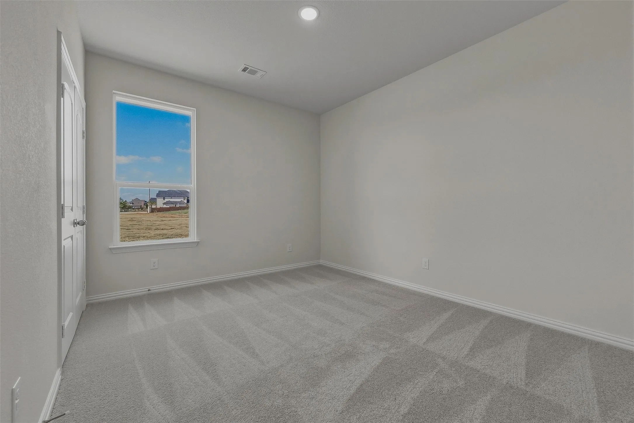 Neutral wall paint, gray carpeting, and a window with a white frame