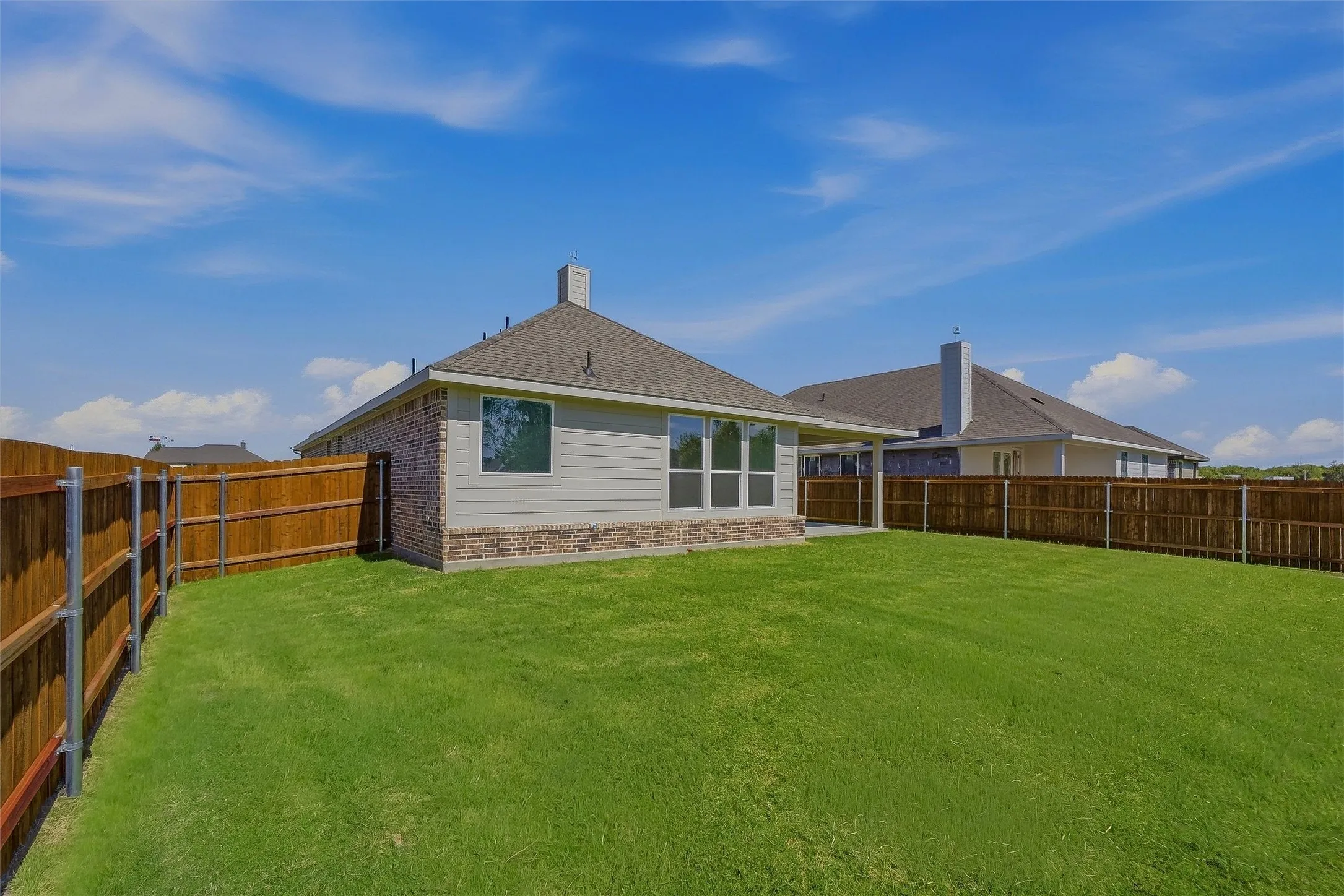 Expansive lawn with a wooden privacy fence, brick and siding exterior, and a covered patio