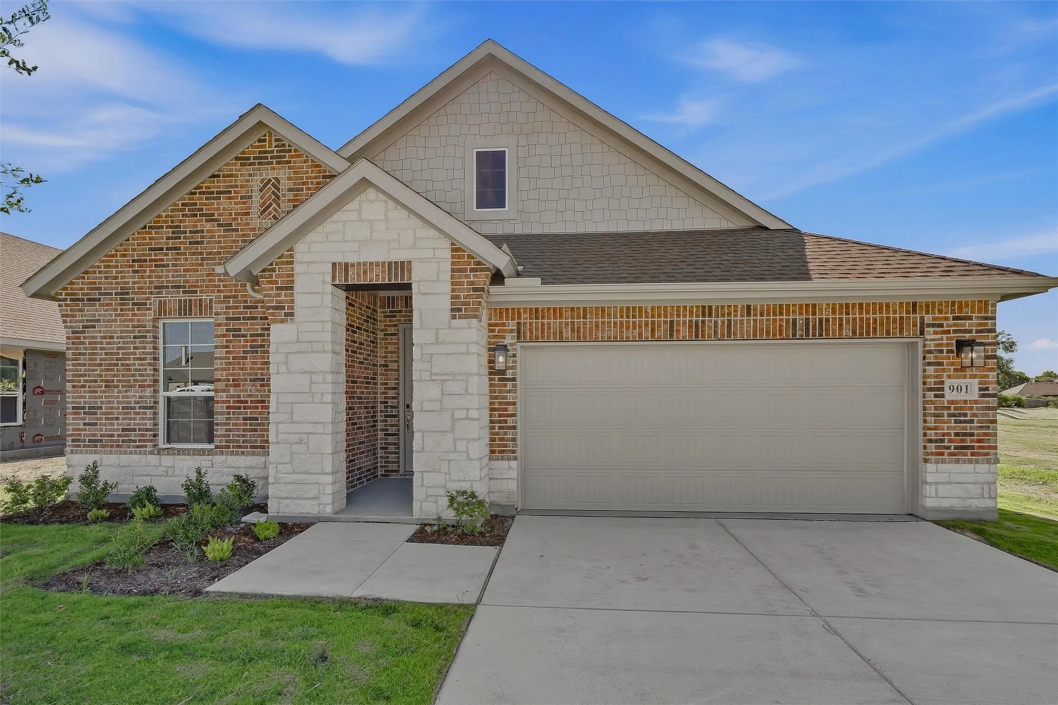 Brick exterior facade with stone accents, covered entry, attached garage, and landscaped front yard