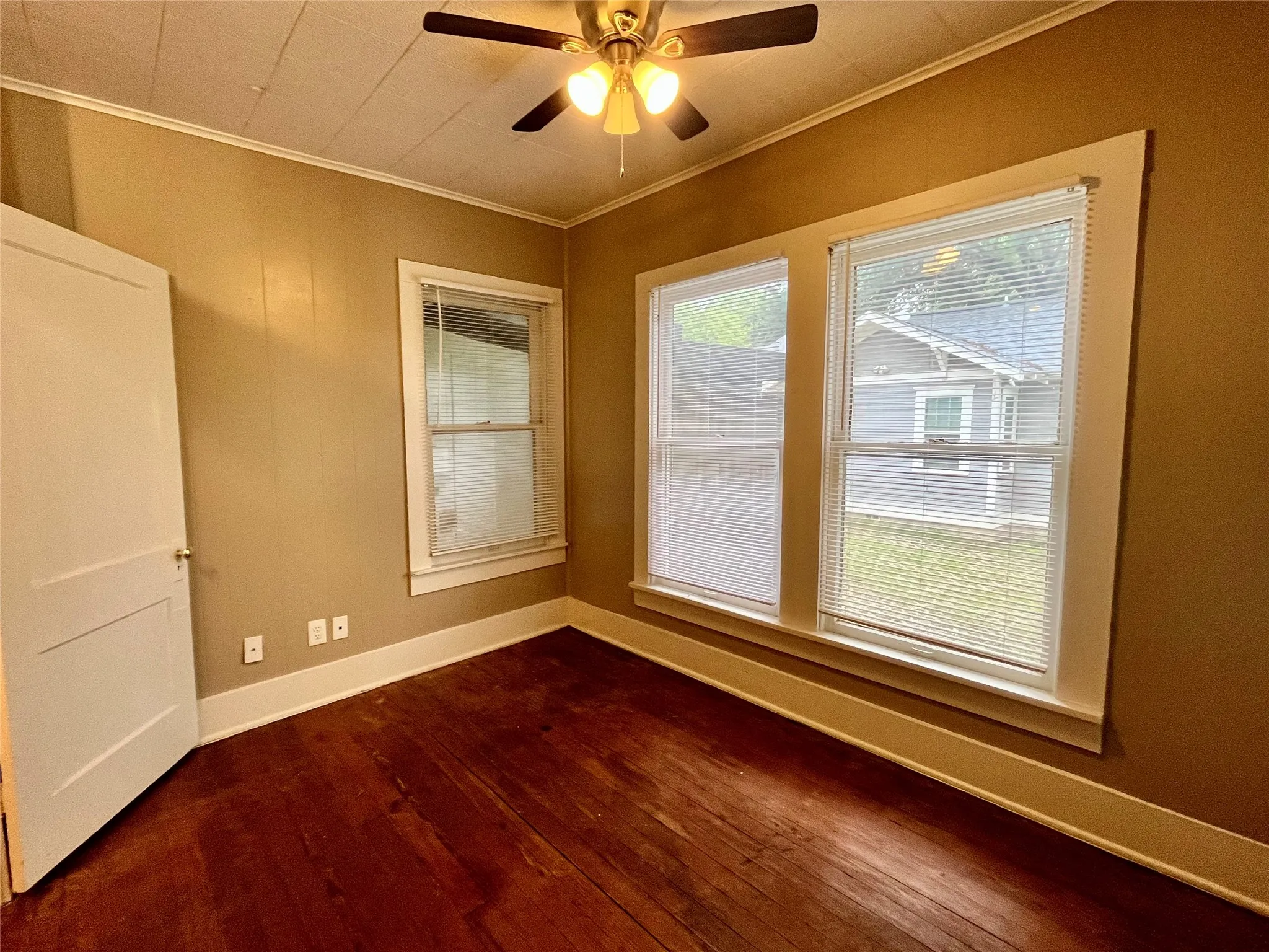 Relax in a sun-drenched bedroom featuring rich wood flooring, a cooling ceiling fan, and large windows that let the natural light pour in.