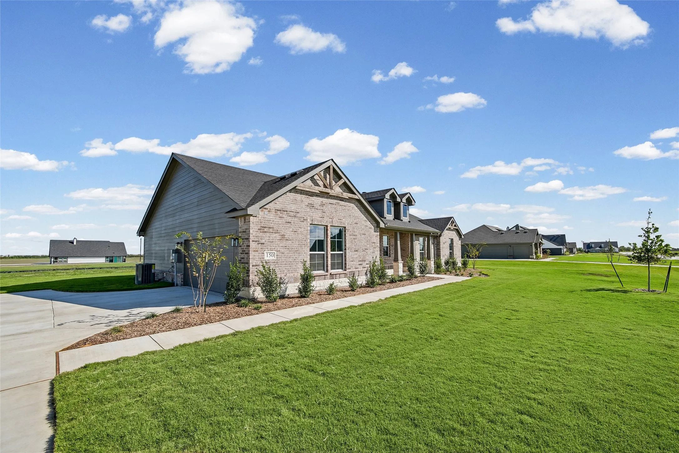 Exterior facade featuring light-toned brick masonry, horizontal siding, decorative gable woodwork, a covered porch, and a concrete driveway