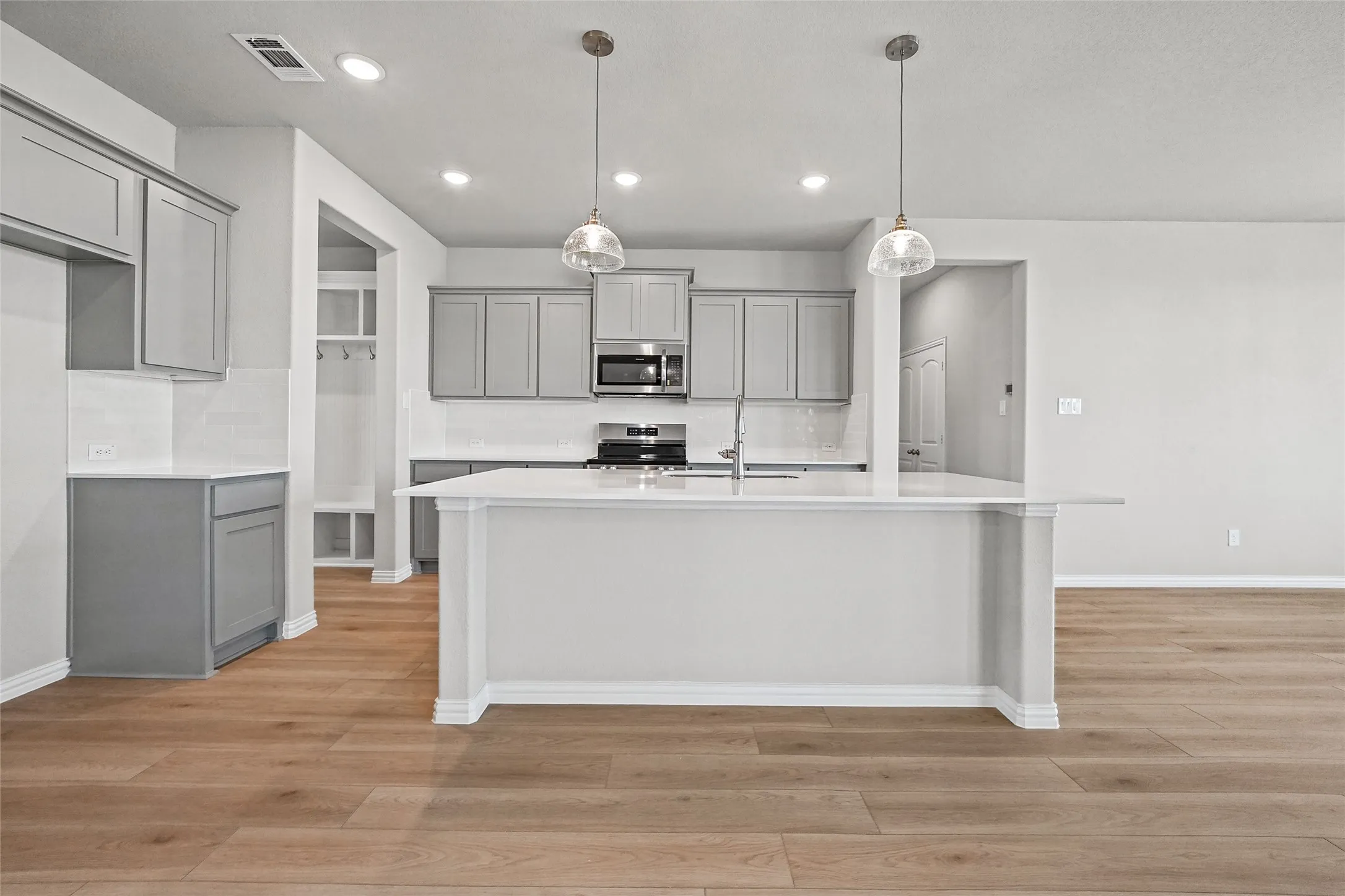 Kitchen featuring a center island with a white countertop, wood-finish flooring, shaker-style grey cabinetry, stainless steel appliances, and dual pendant lighting