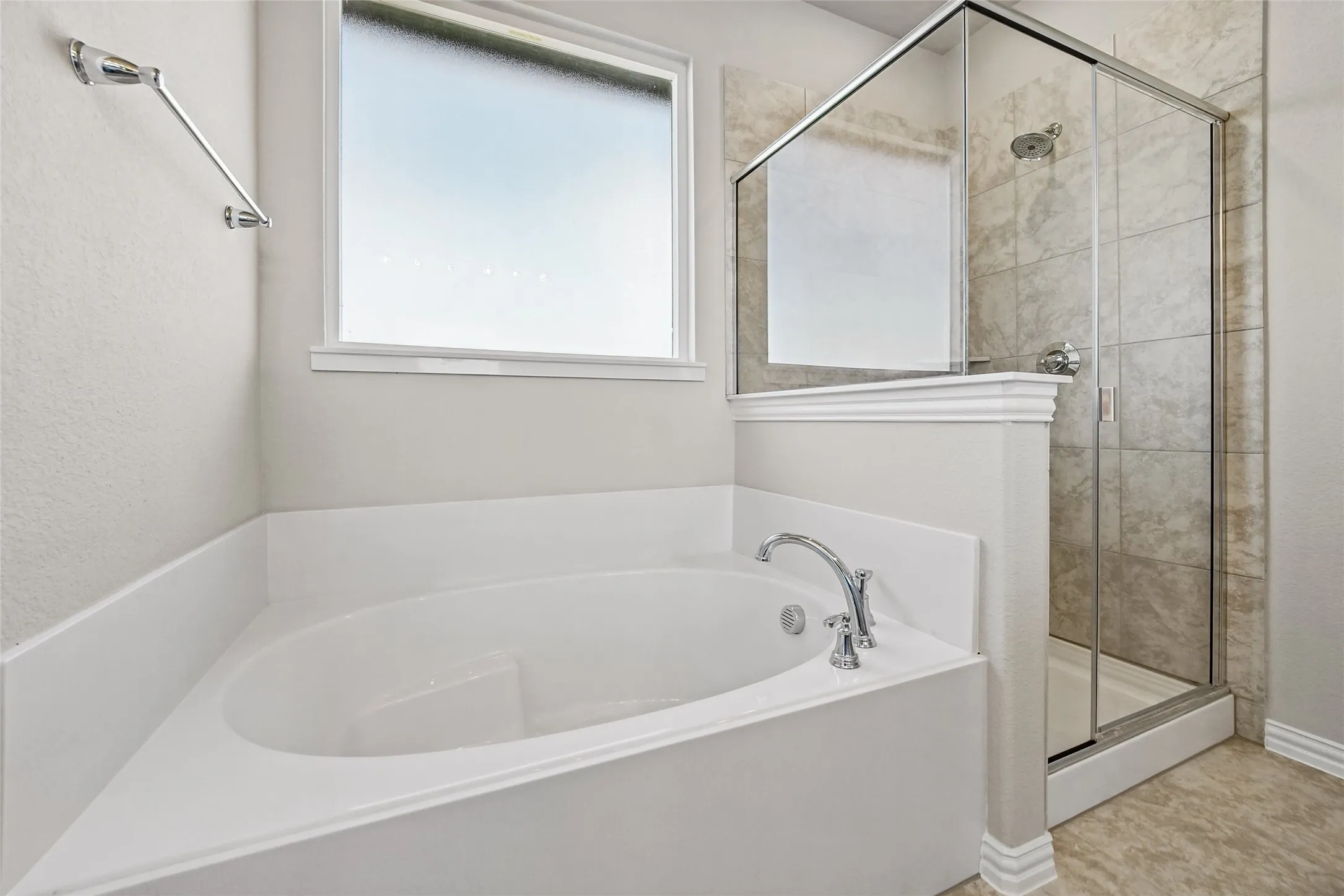 Oval soaking tub with chrome fixtures, glass-enclosed shower with tiled surround, and frosted window