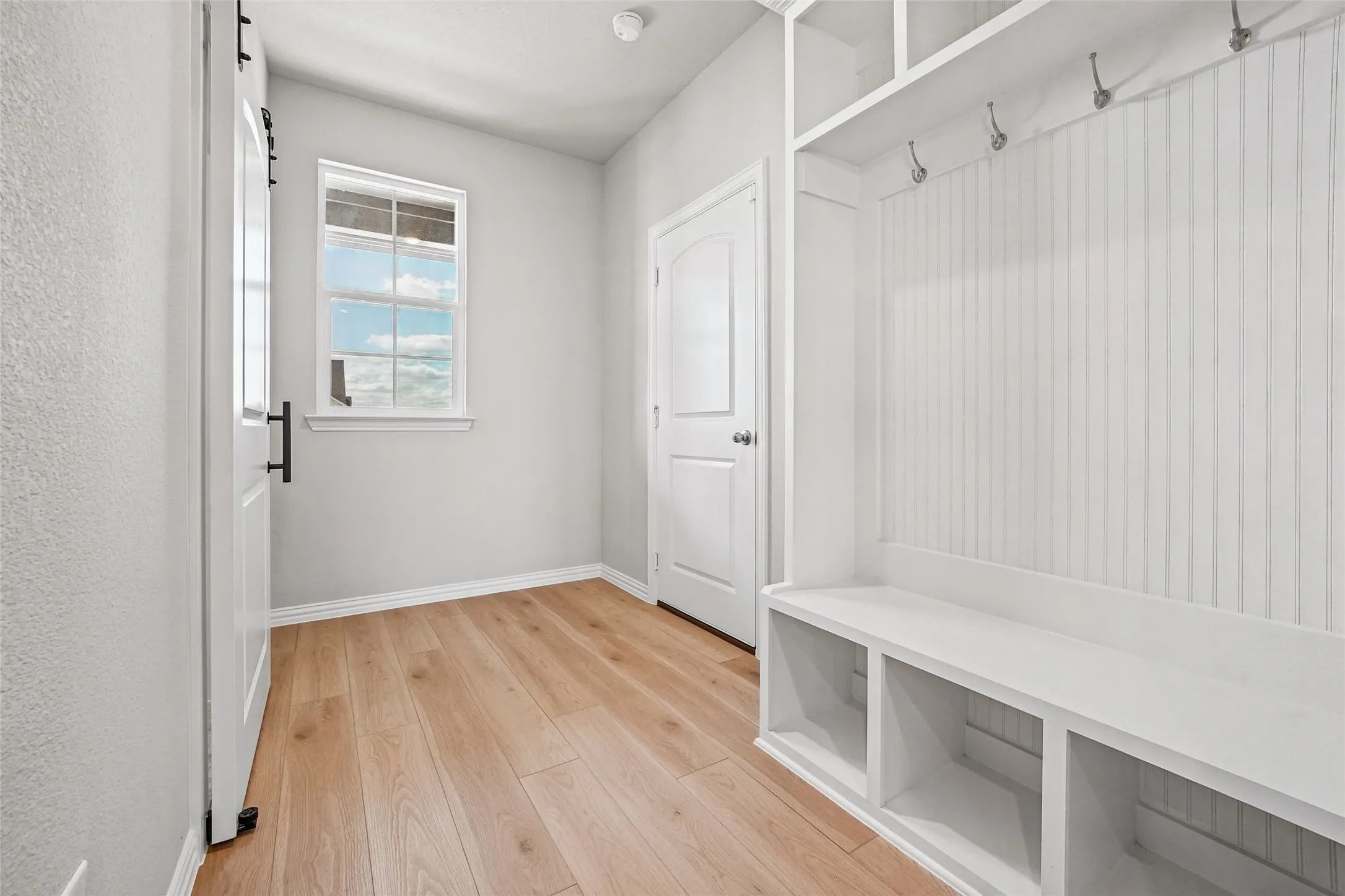 Built-in mudroom cabinetry featuring beadboard paneling, integrated storage cubbies, and overhead metal hooks, complemented by wood-finish flooring and a single-hung window