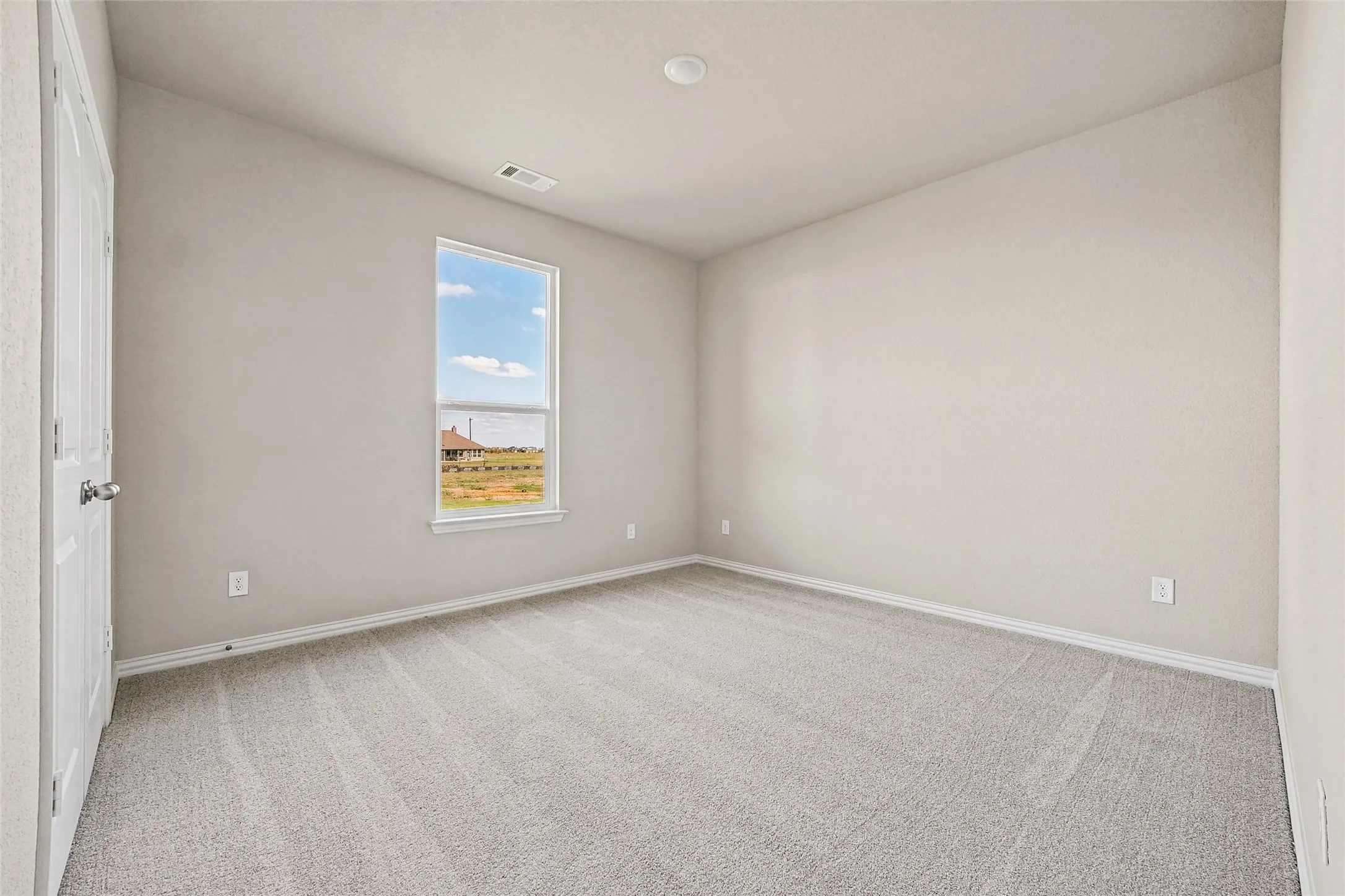 Neutral-toned interior space featuring light-colored wall paint, plush carpeting, a single-hung window, and a paneled interior door