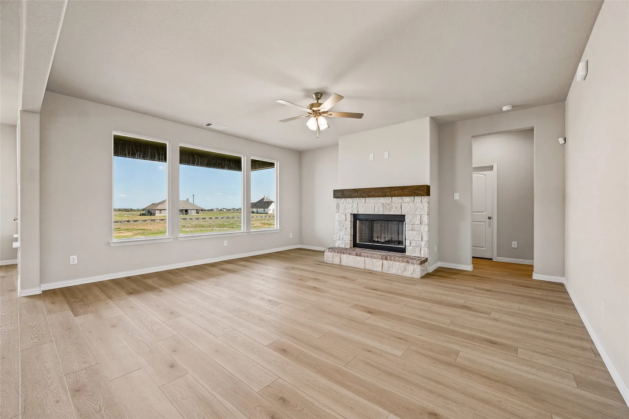 Living area featuring wood-finish flooring, stone-surround fireplace with a wooden mantel, and a ceiling fan