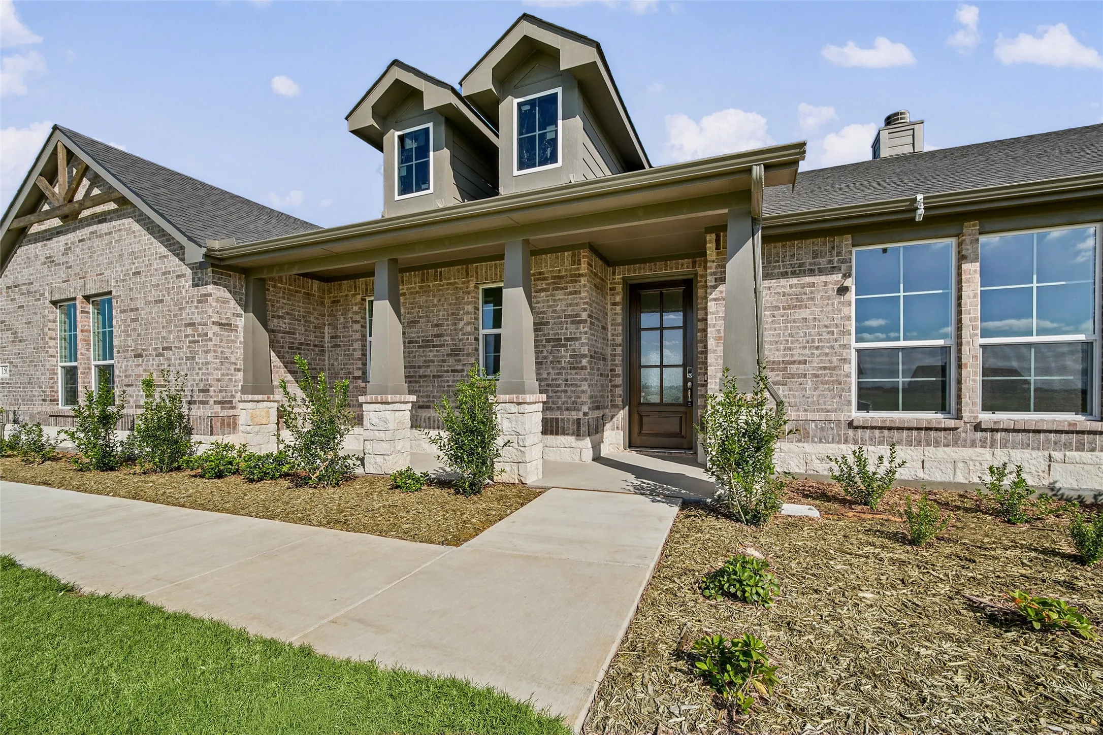 Brick and stone exterior featuring a covered front porch, dual dormers, and multi-pane windows