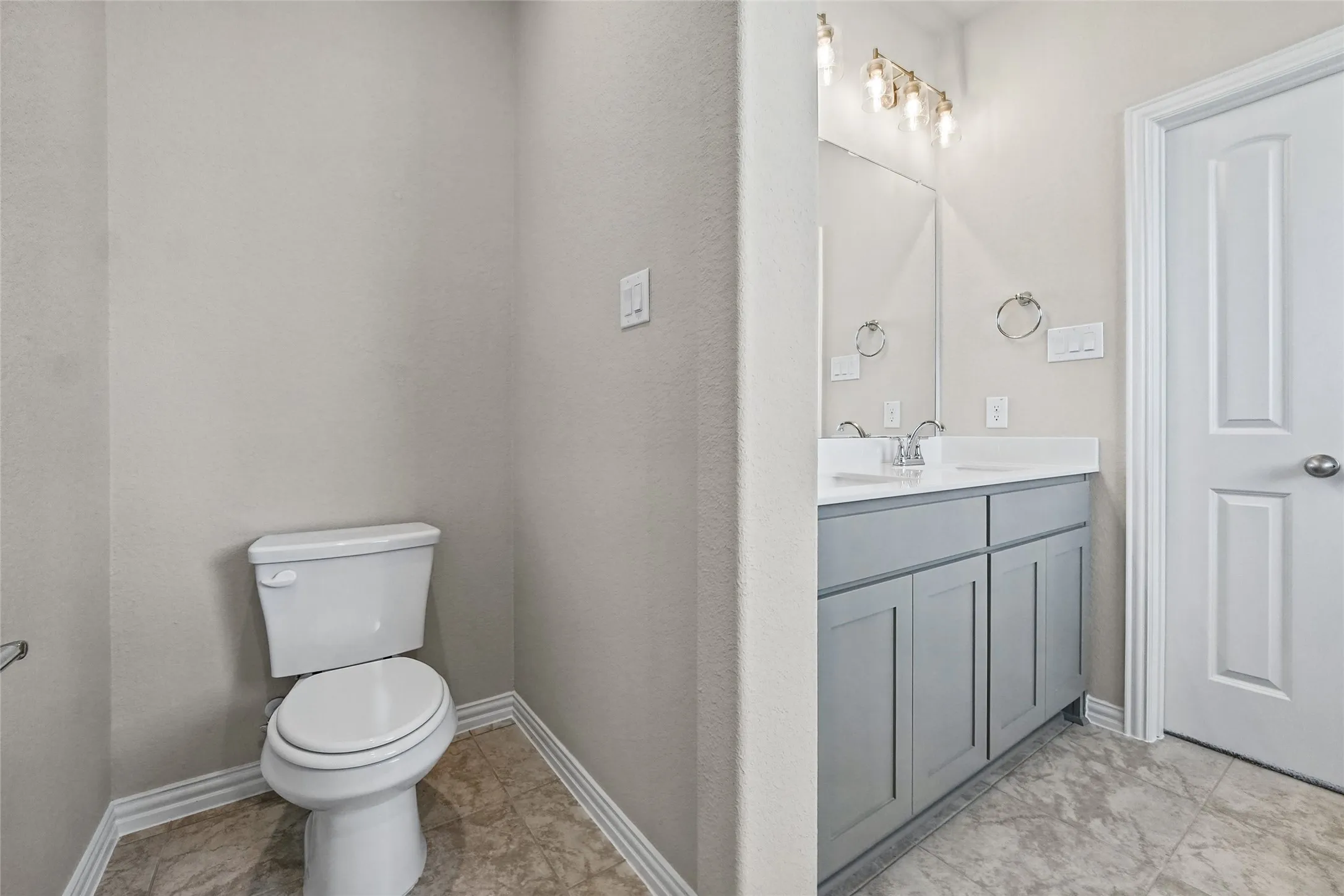 Shaker-style grey vanity with a solid surface countertop, undermount sink, multi-bulb wall-mounted light fixture, and tile flooring