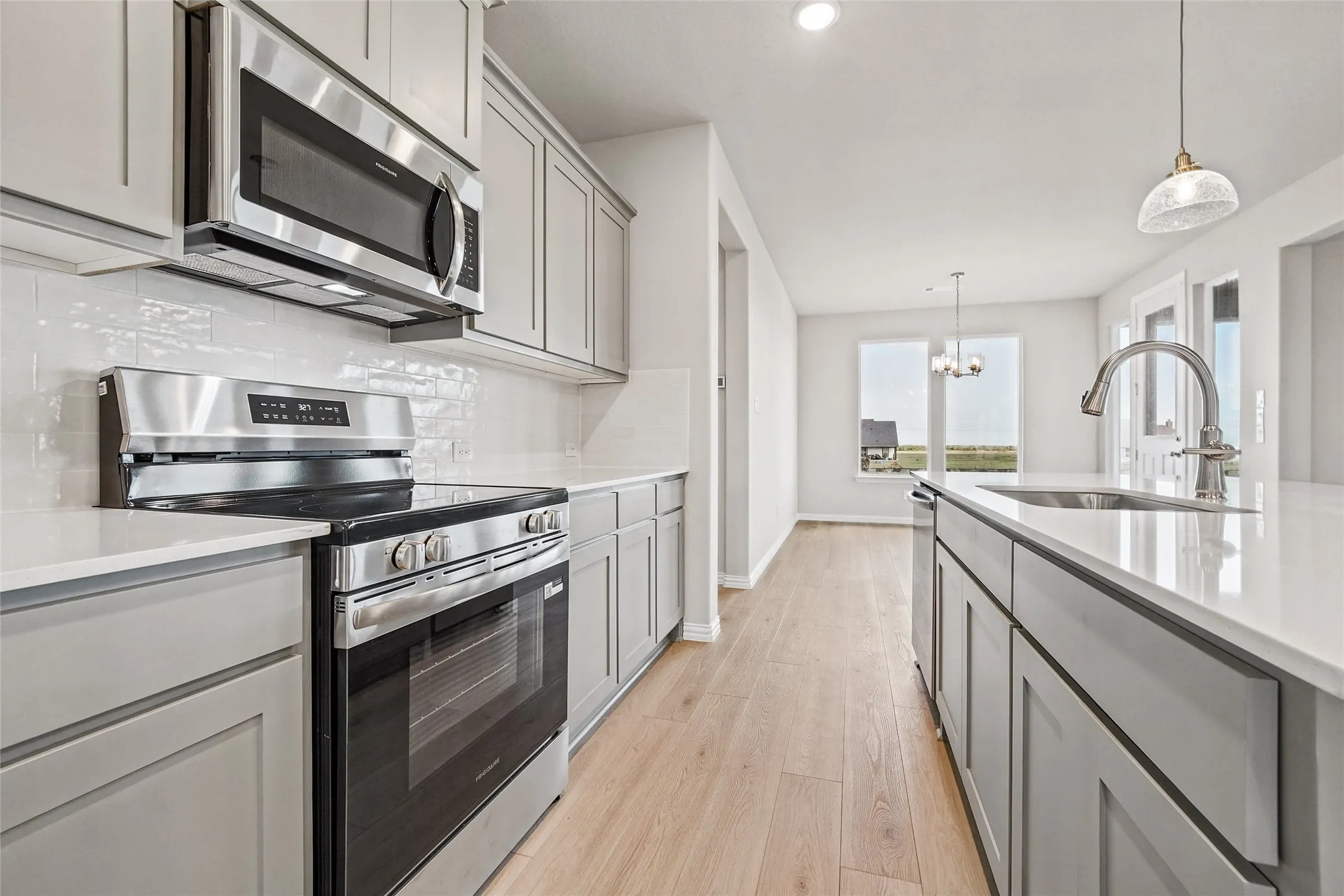 Kitchen featuring stainless steel appliances, quartz countertops, subway tile backsplash, shaker-style cabinetry, and wood-finish flooring