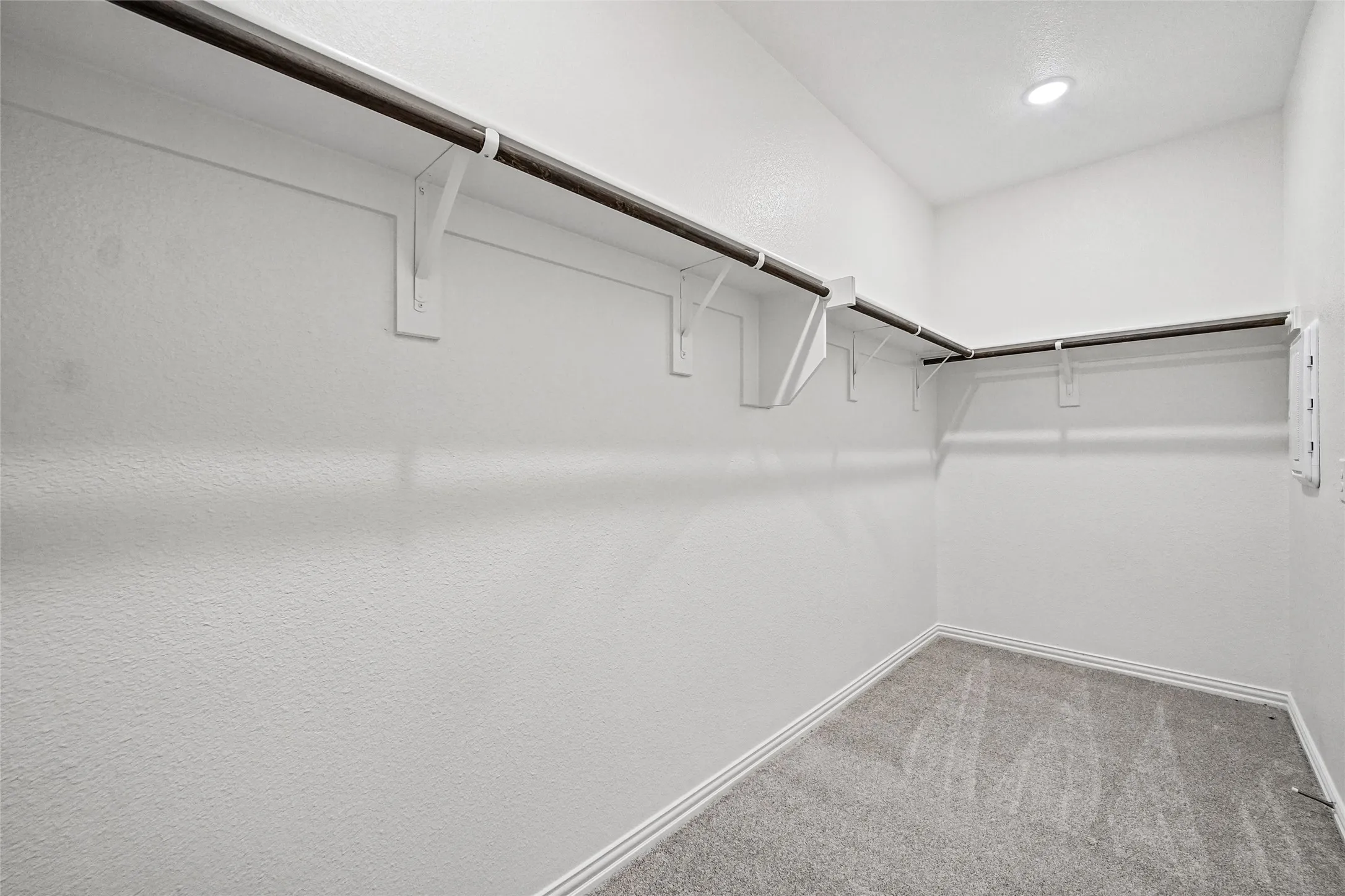Walk-in closet featuring wall-to-wall carpeting, tiered built-in shelving, and dual hanging rods