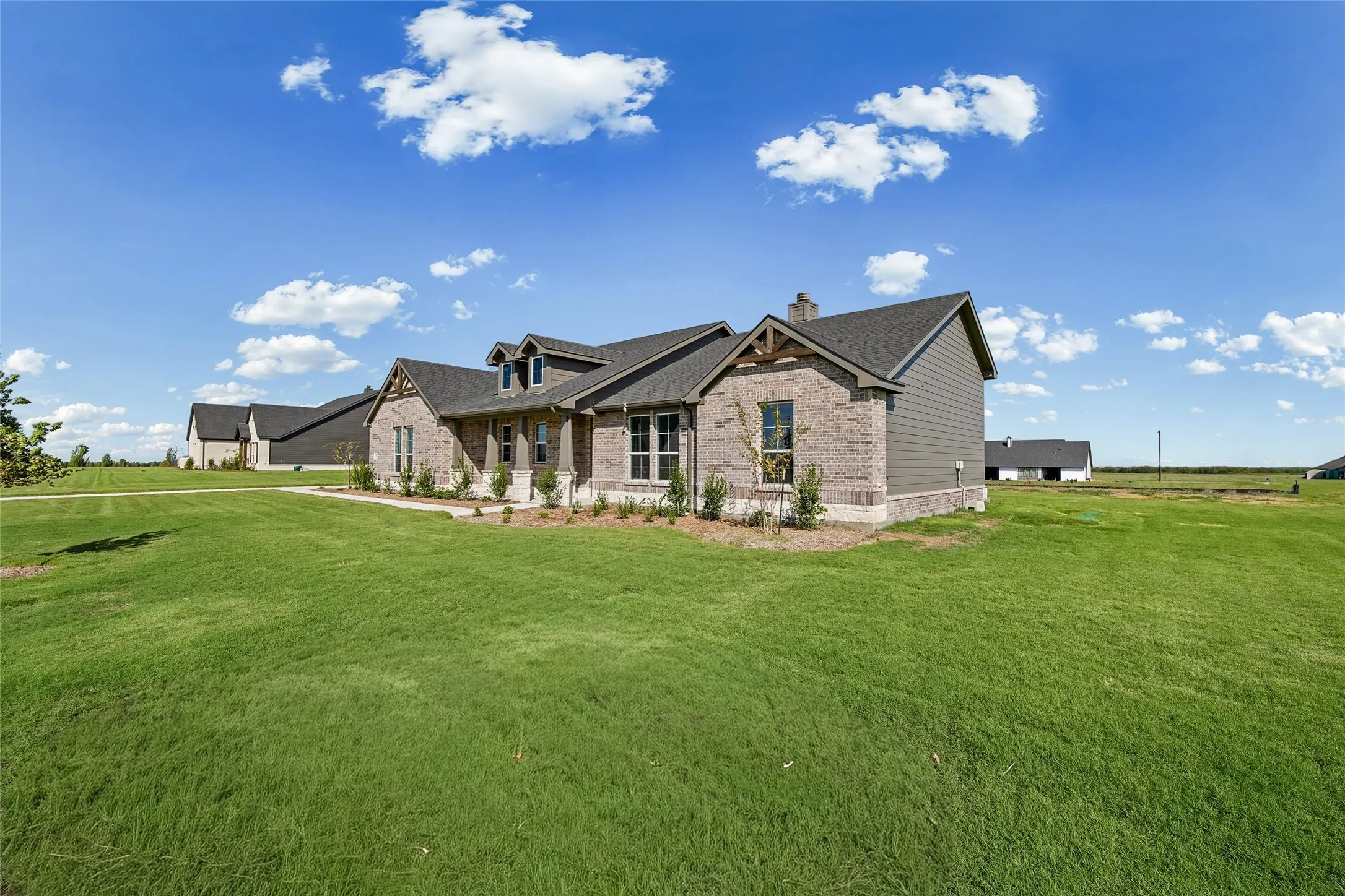 Single-story residence featuring a brick and horizontal siding exterior, multi-gabled roofline with timber corbel accents, and an expansive surrounding lawn