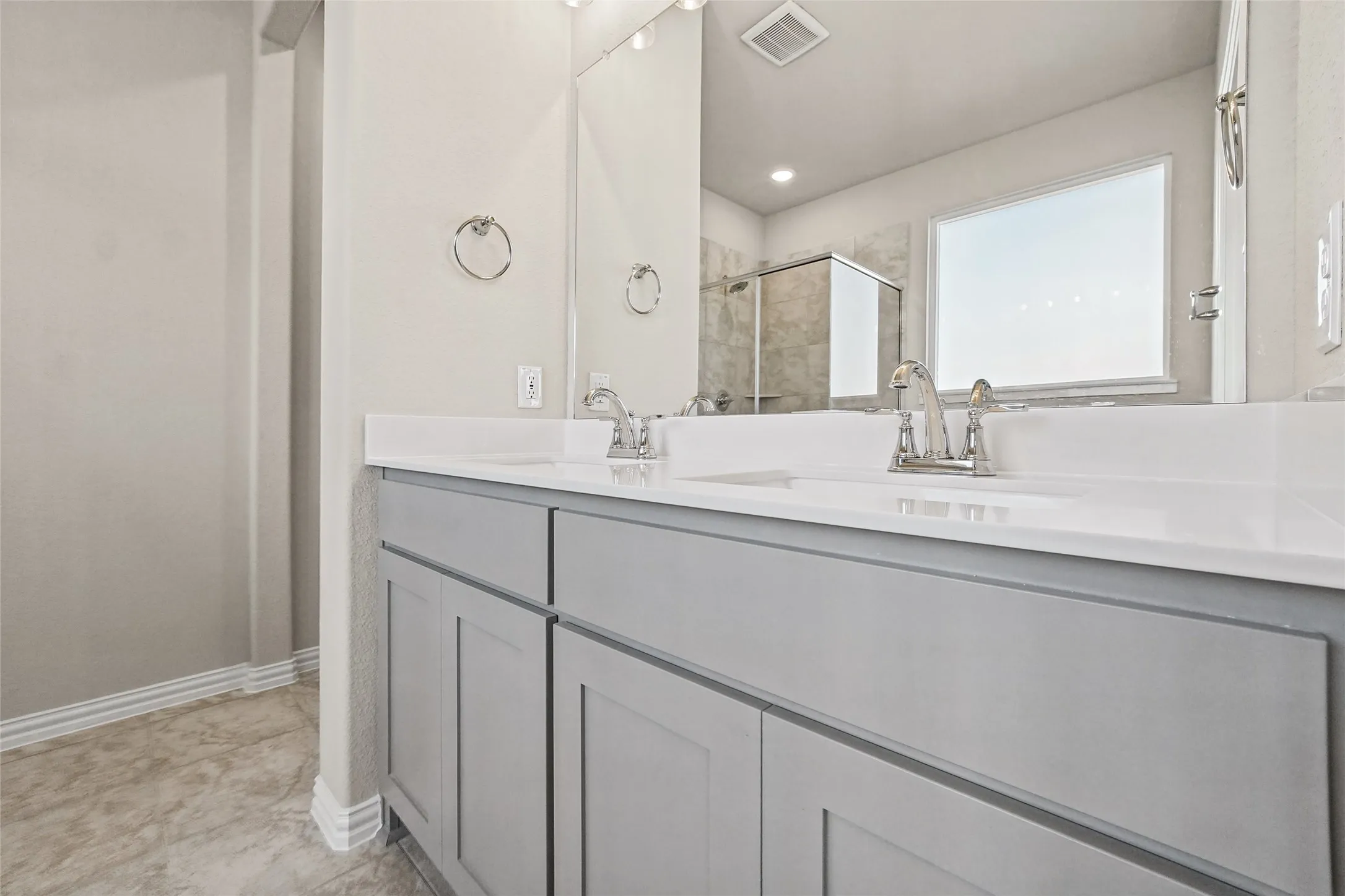 Dual vanity featuring a white solid-surface countertop, recessed-panel grey cabinetry, integrated sinks with polished chrome faucets, and a large plate-glass mirror