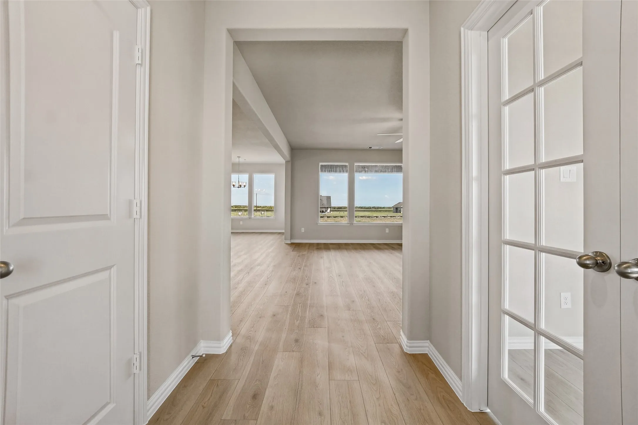 Interior hallway featuring wood-finish flooring, paneled interior doors, and glass-paneled French doors with brushed metal hardware