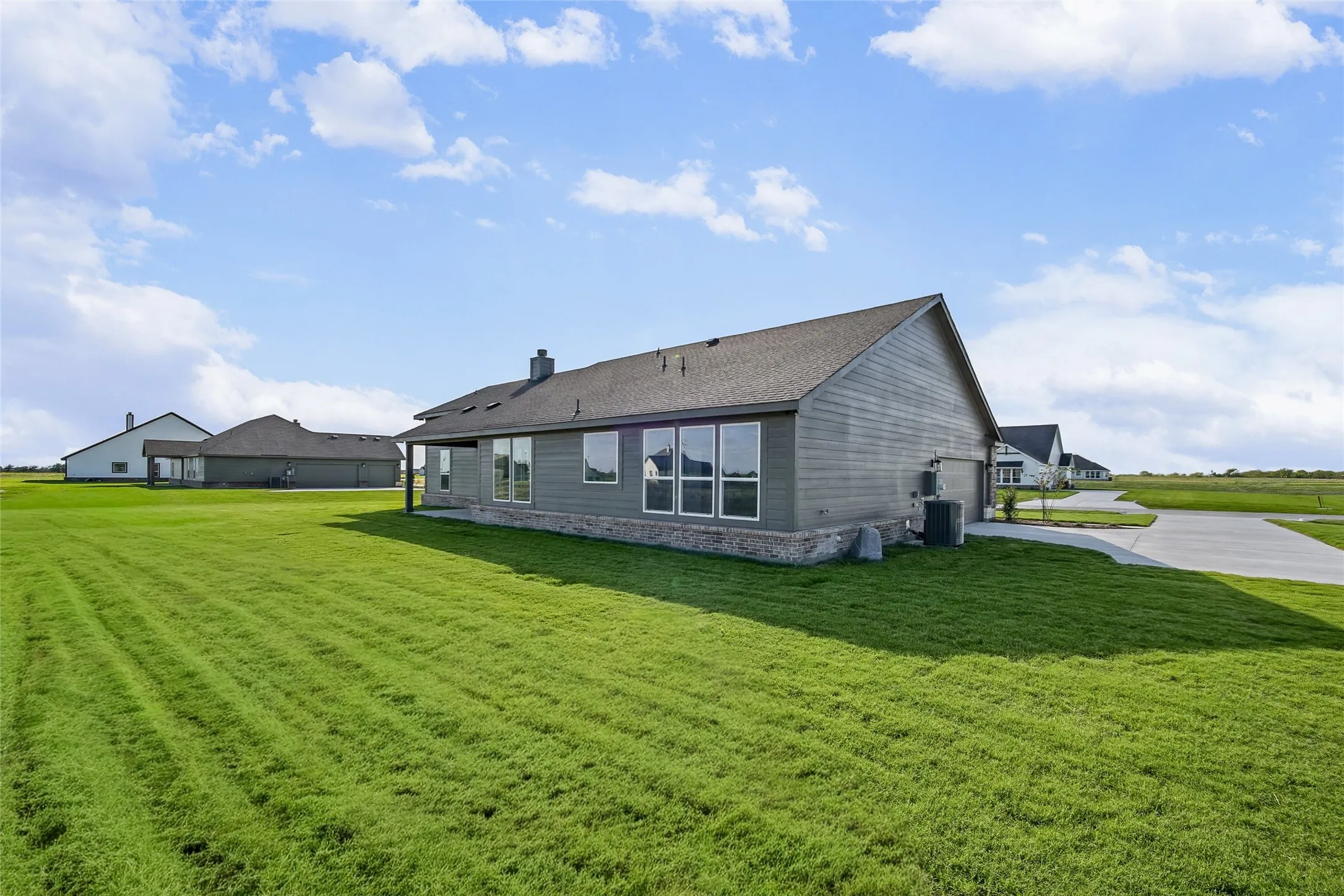 Exterior featuring horizontal siding, stone veneer accents, an asphalt shingle roof, large windows, and a concrete driveway