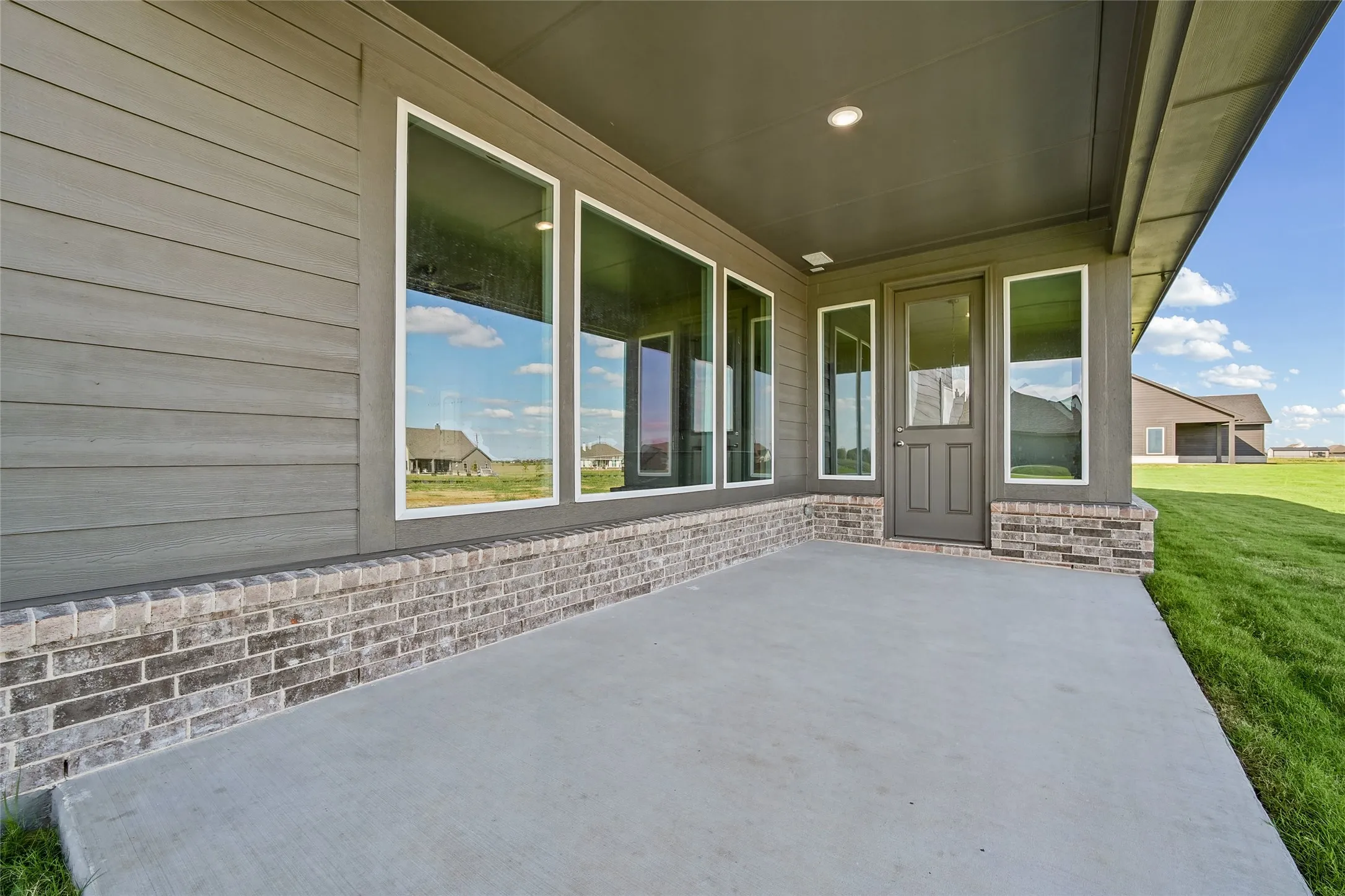 Covered concrete patio featuring lap siding, brick masonry detailing, recessed ceiling lighting, and large picture windows