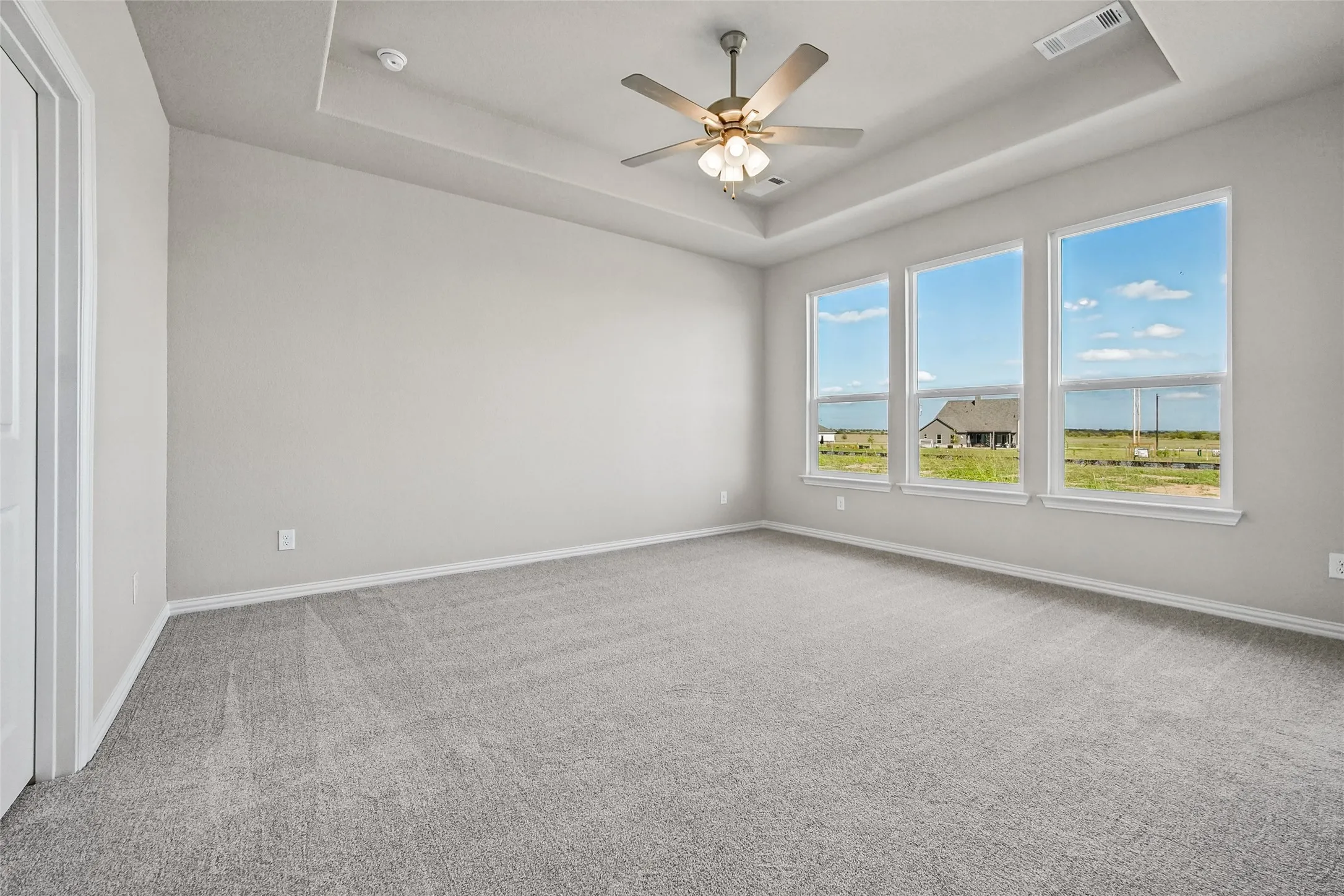Tray ceiling featuring a central brushed-metal ceiling fan with integrated lighting, wall-to-wall carpeting, and triple windows providing natural light
