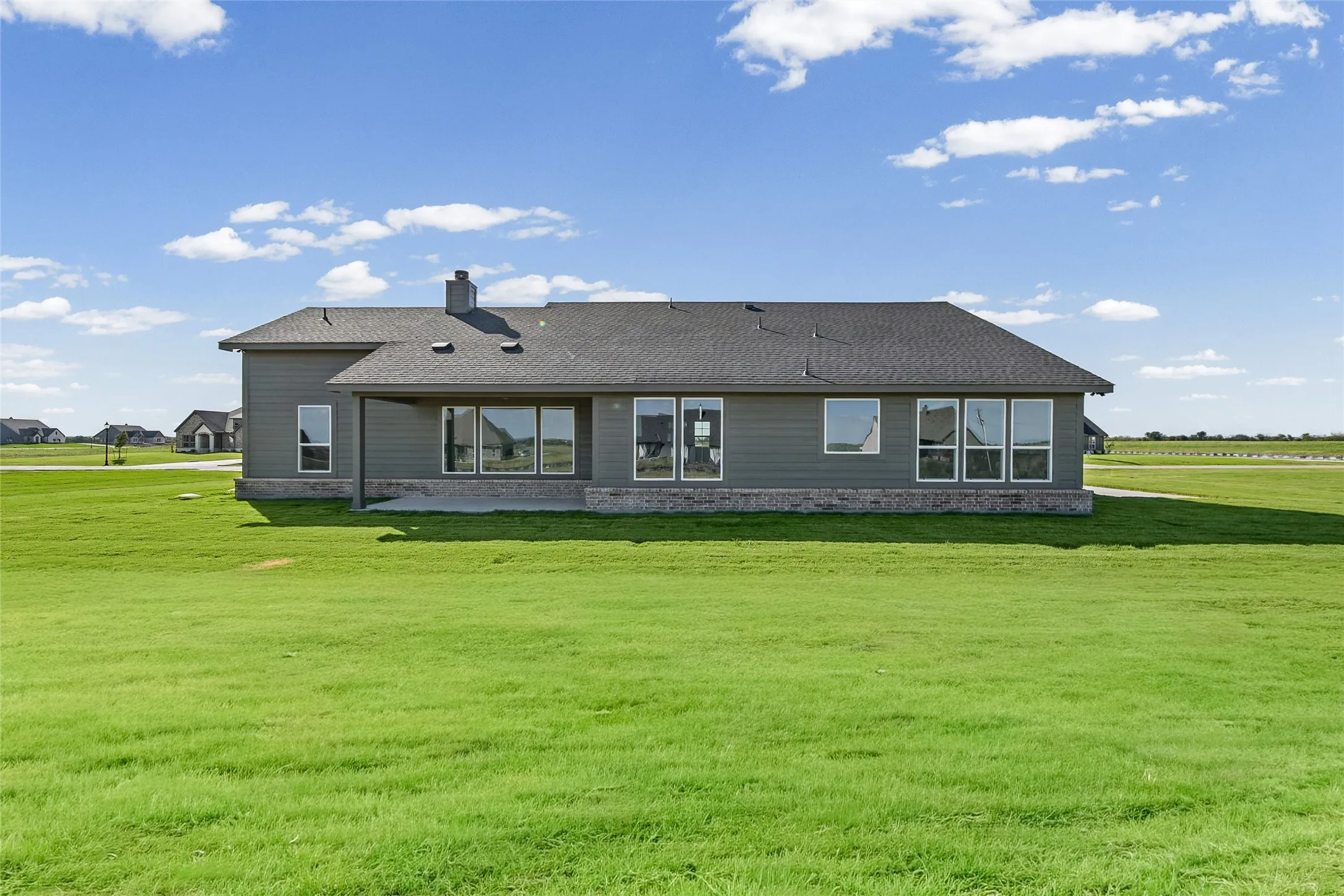 Single-story residence featuring horizontal lap siding, brick veneer masonry, a covered rear patio, multiple large windows, and a sprawling lawn