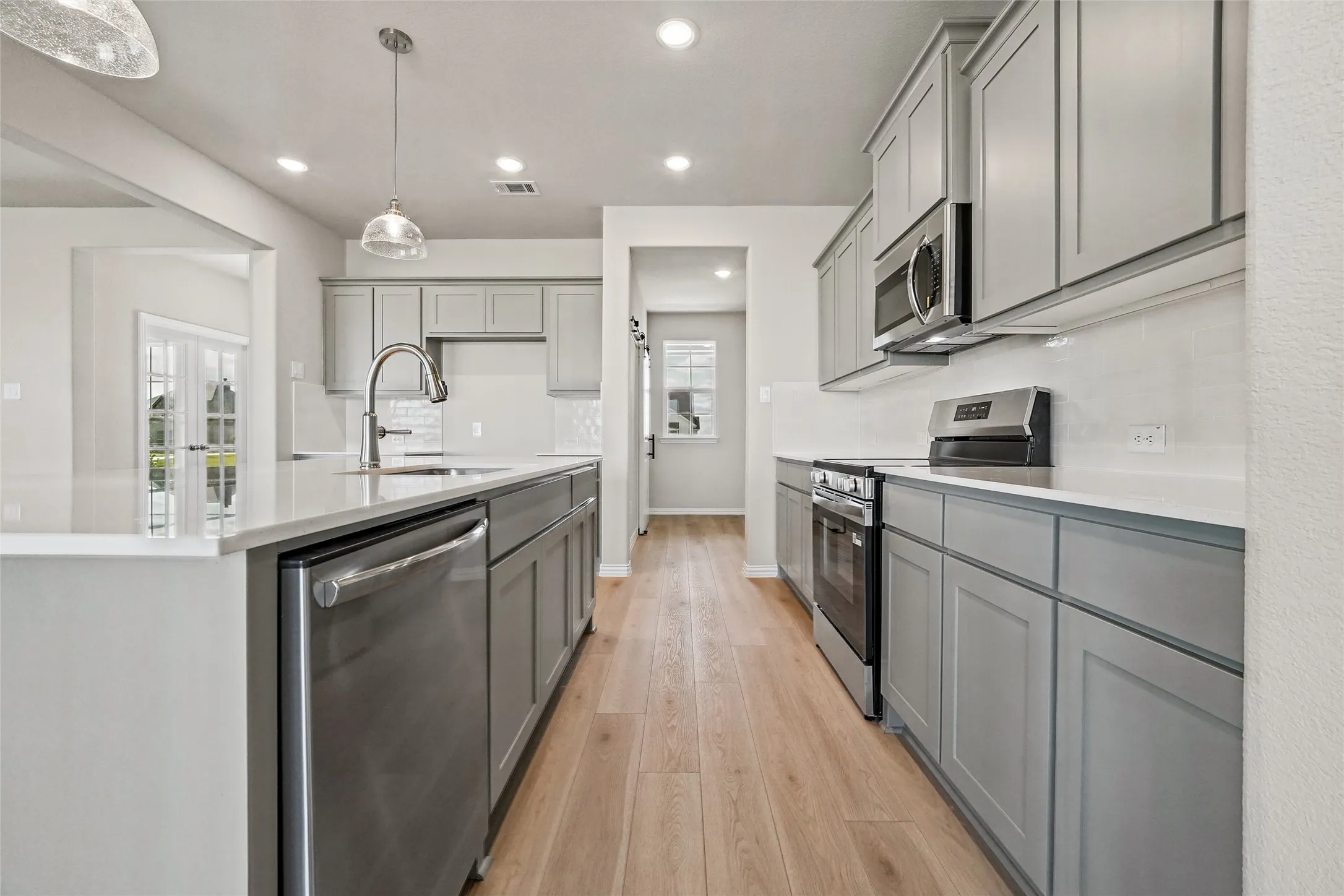 Kitchen featuring gray shaker-style cabinetry, quartz countertops, stainless steel appliances, white subway tile backsplash, and wood-finish flooring