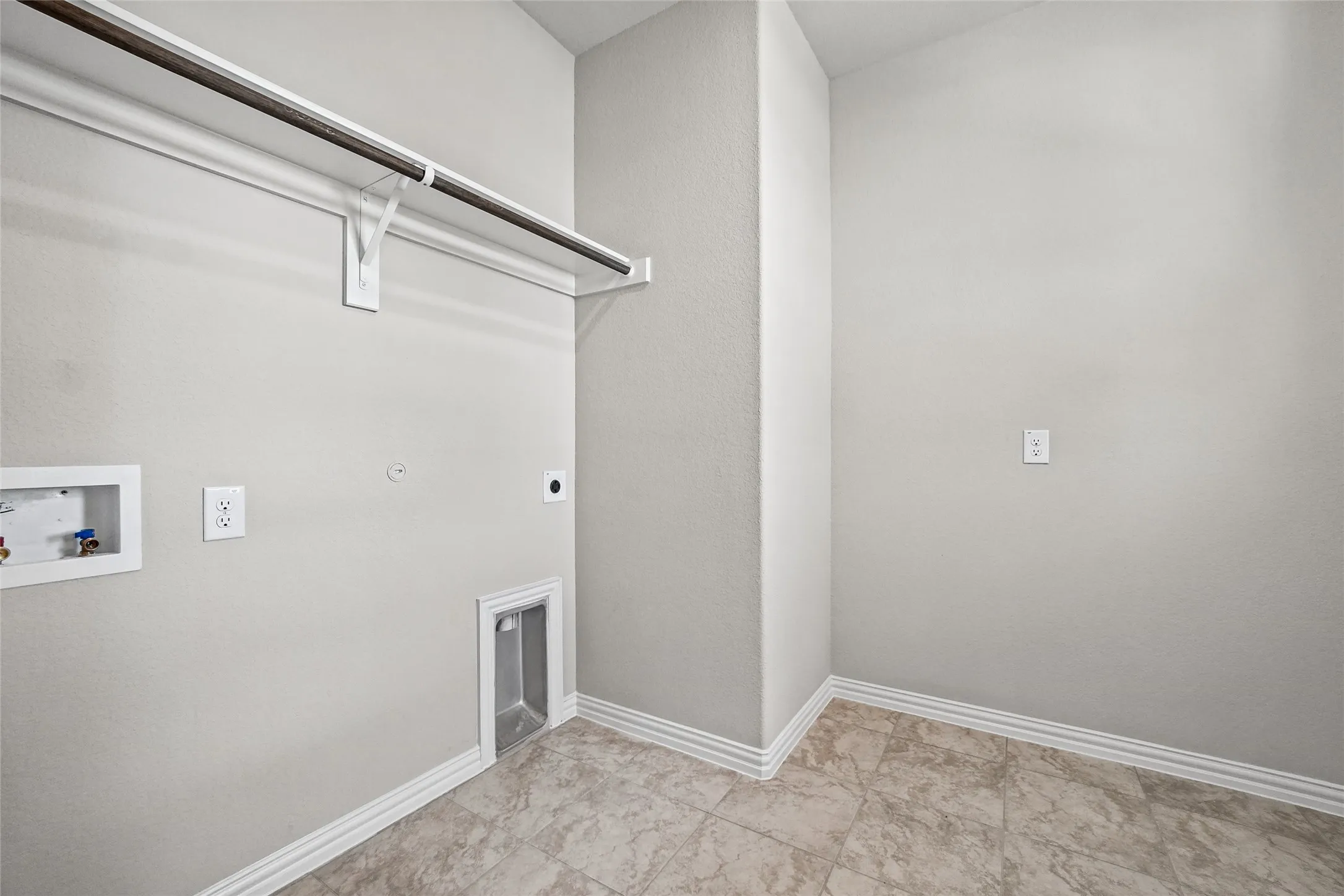 Utility area featuring tile flooring, built-in metal hanging rod, and recessed water and drain connections