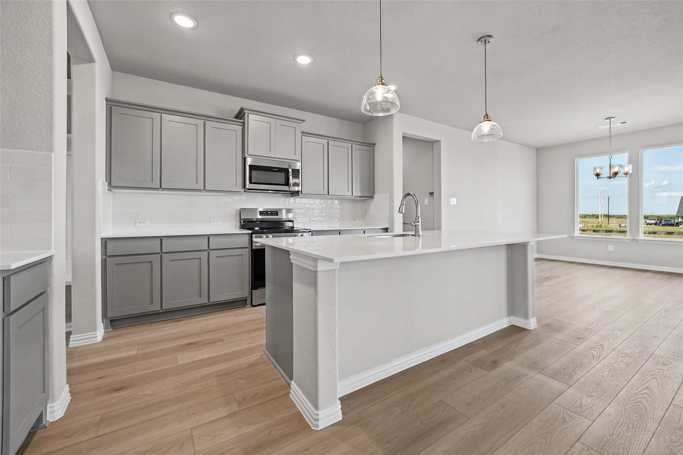 Kitchen featuring grey shaker-style cabinetry, quartz countertops, subway tile backsplash, stainless steel appliances, and wood-finish flooring