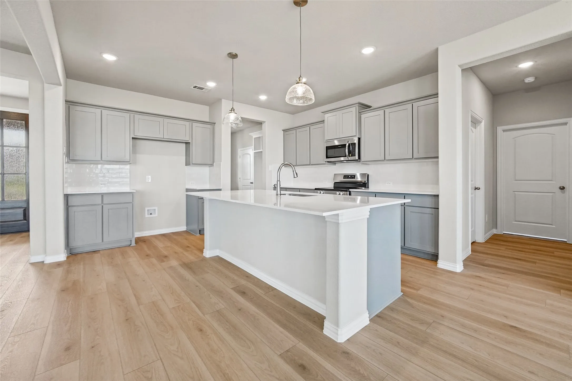 Kitchen featuring grey shaker-style cabinetry, quartz countertops, a central island with a stainless steel faucet, wood-finish flooring, and recessed lighting