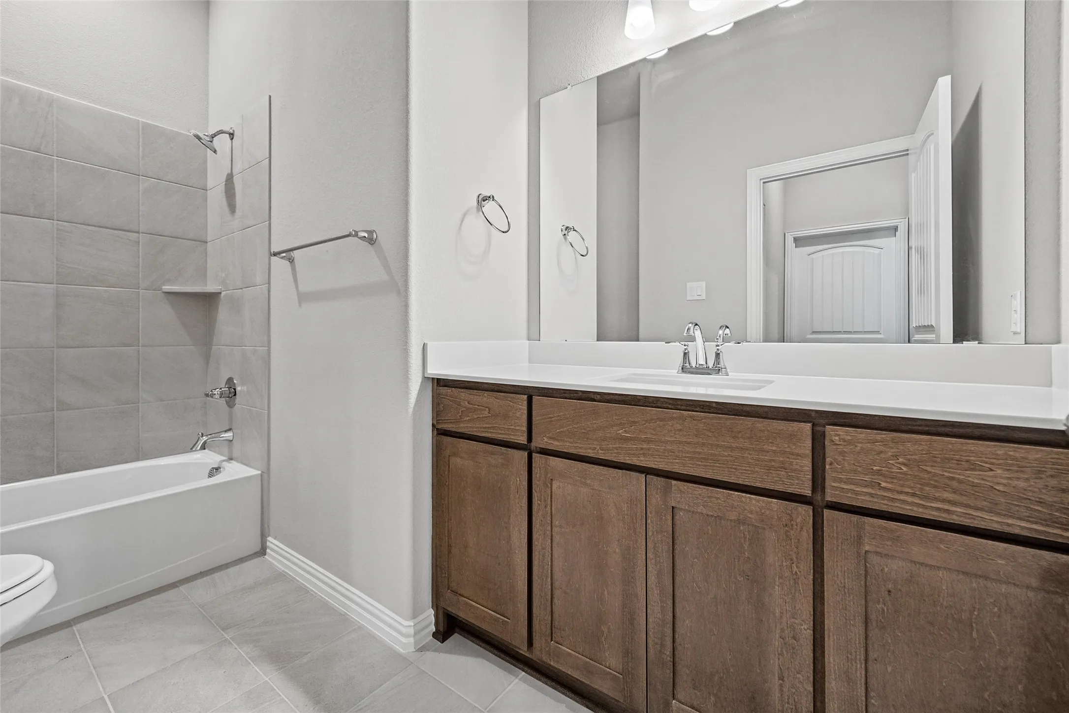 Integrated bathtub with tiled shower surround, single vanity with wood-finish cabinetry, white countertop, and large mirror