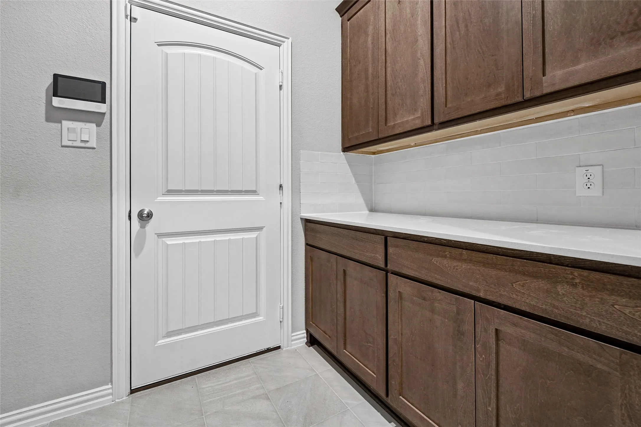 Wood-finish cabinetry with white countertops, subway tile backsplash, and light-toned tile flooring