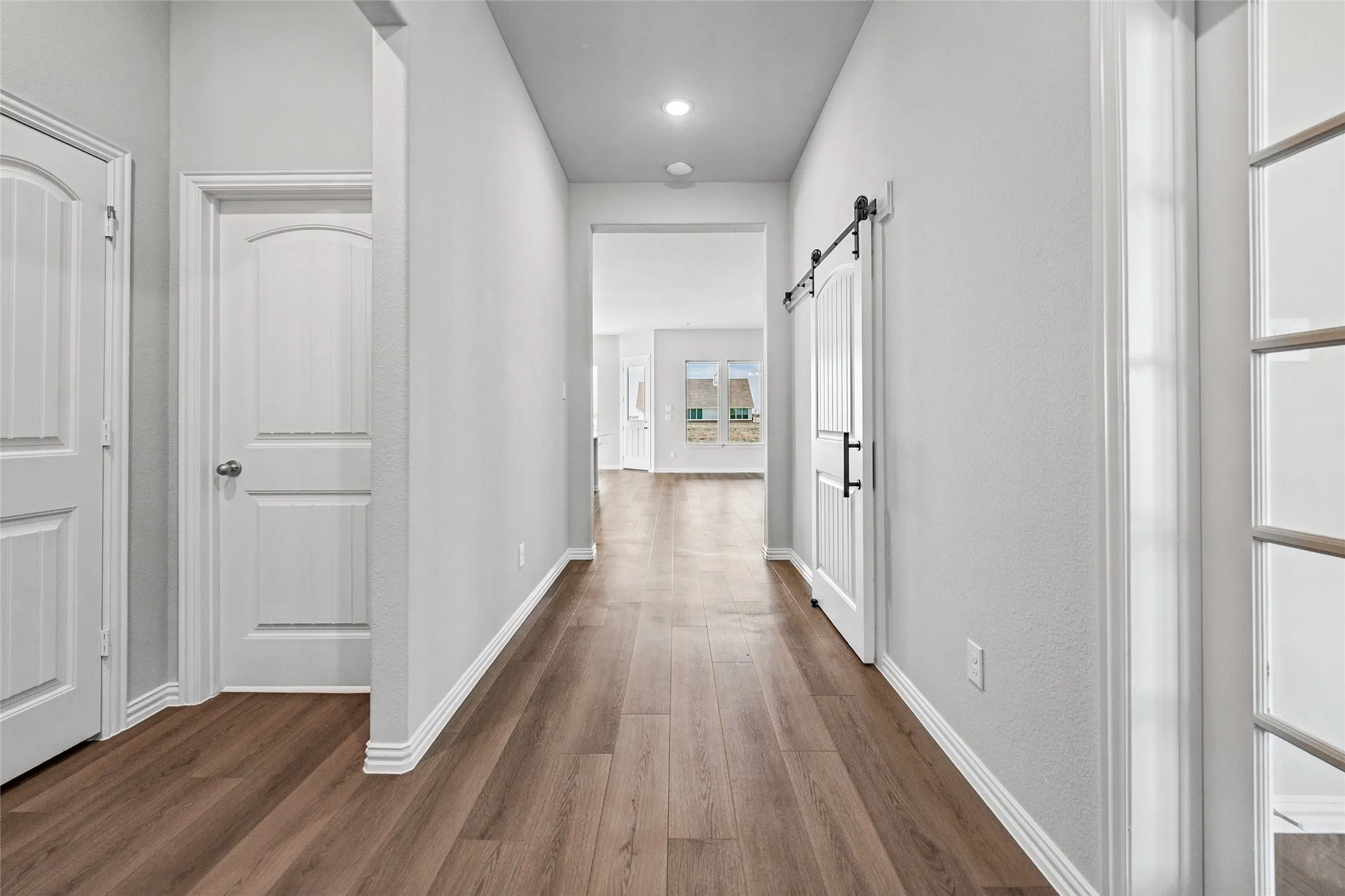 Wood-finish flooring throughout, white trim, recessed lighting, and a white barn door with black hardware