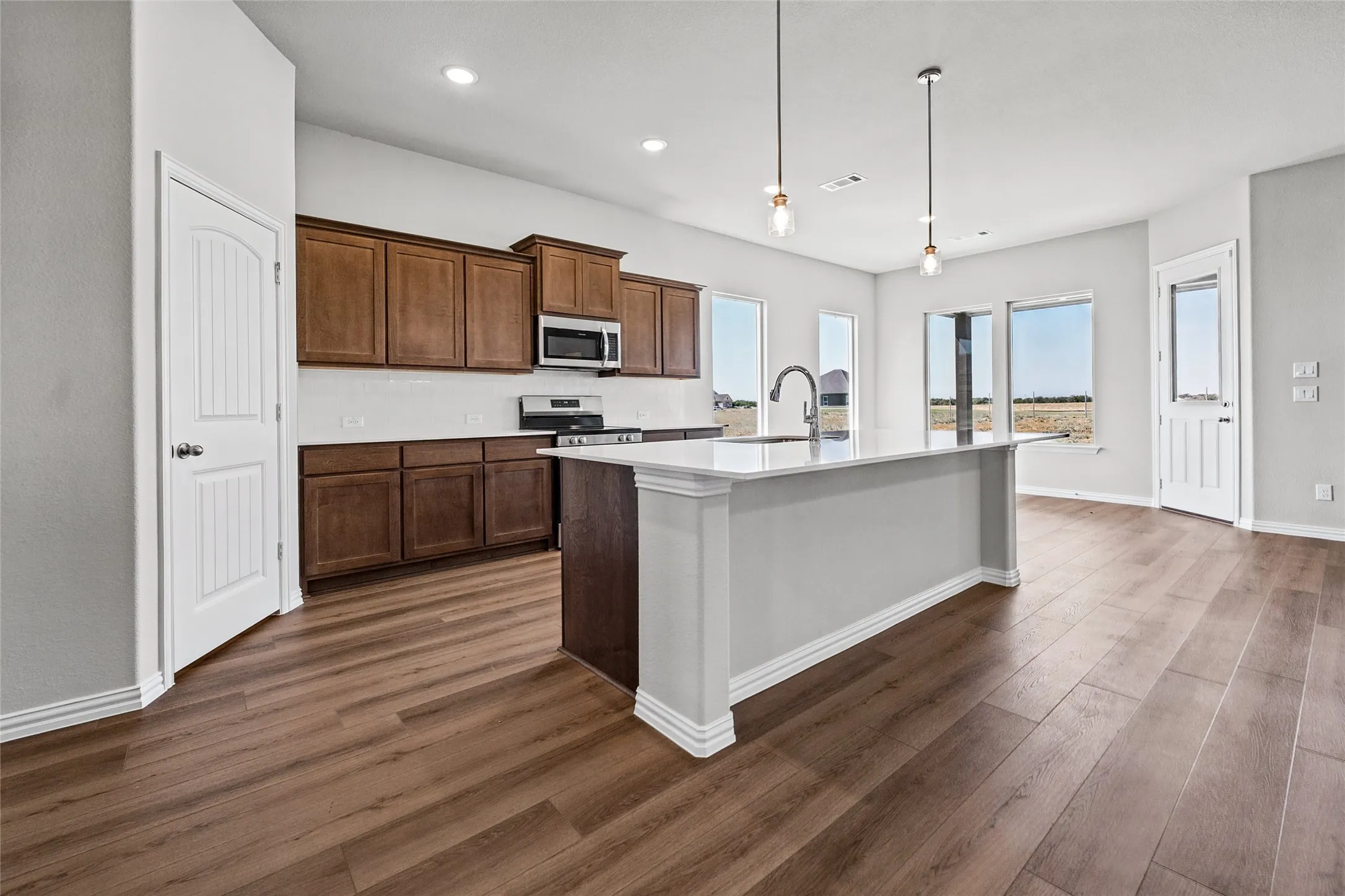 Kitchen featuring wood-finish flooring, white countertops, dark wood cabinetry, stainless steel appliances, and pendant lighting