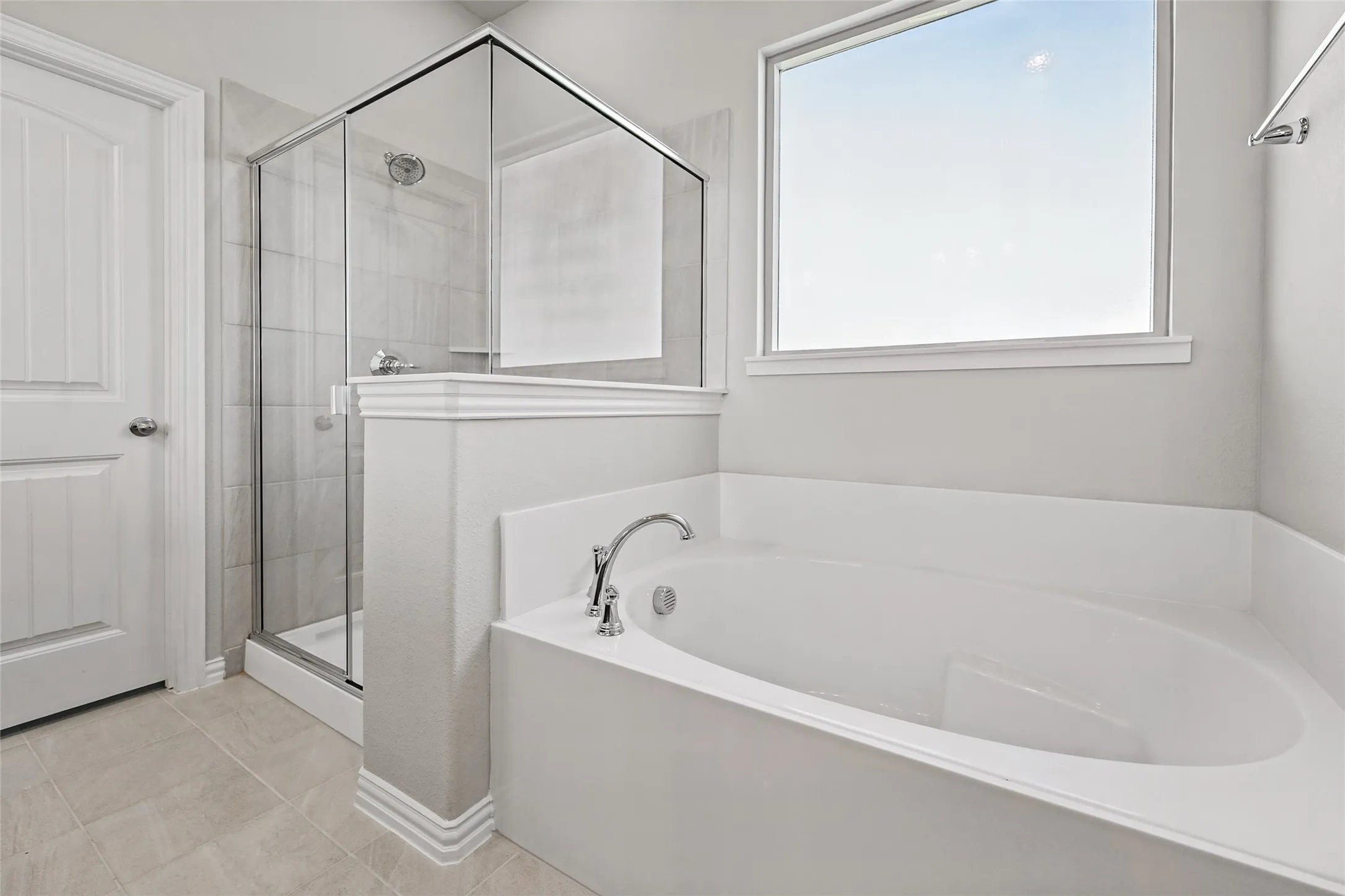 Soaking tub with chrome fixtures, glass-enclosed shower, tile flooring, and a large window