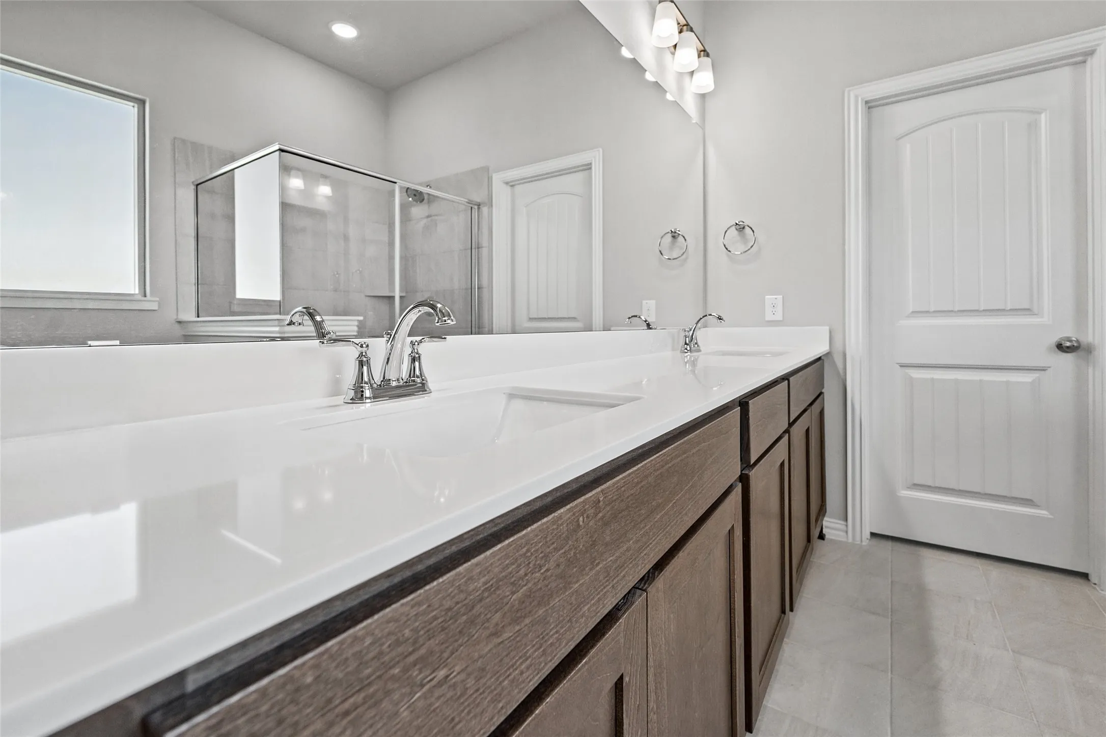 Dual vanity with integrated sinks, wood-finish cabinetry, chrome fixtures, and a framed glass shower enclosure