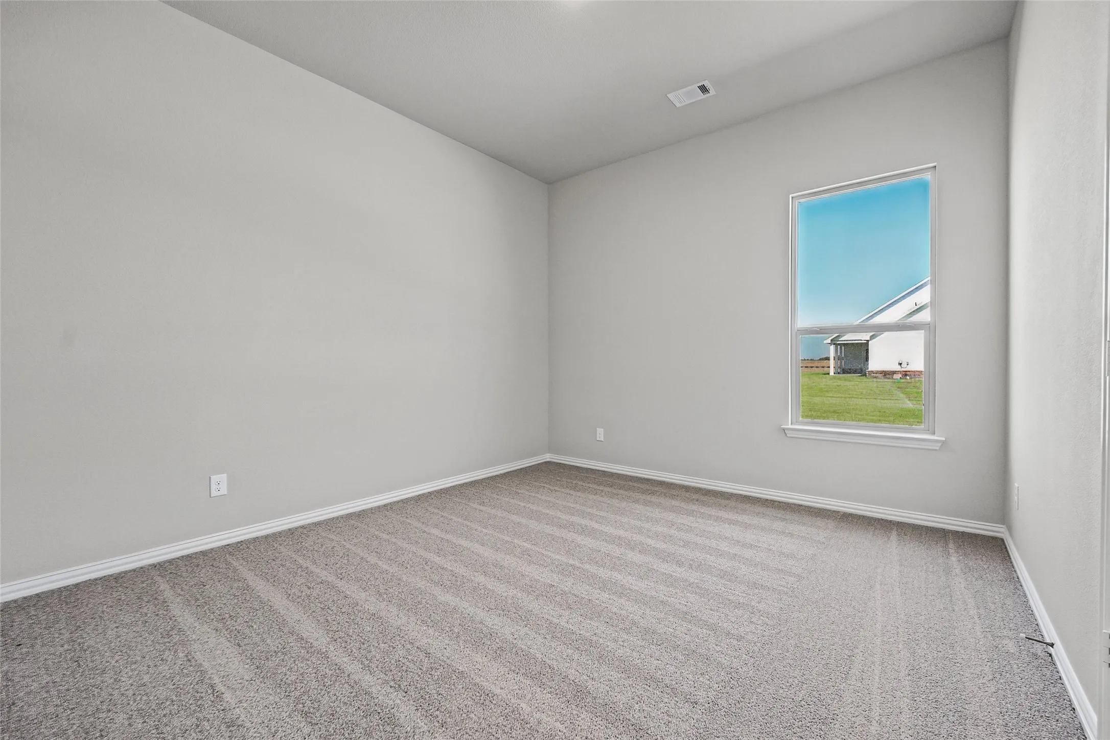 Spacious room featuring neutral paint, light-toned carpeting, a single window, and vaulted ceilings