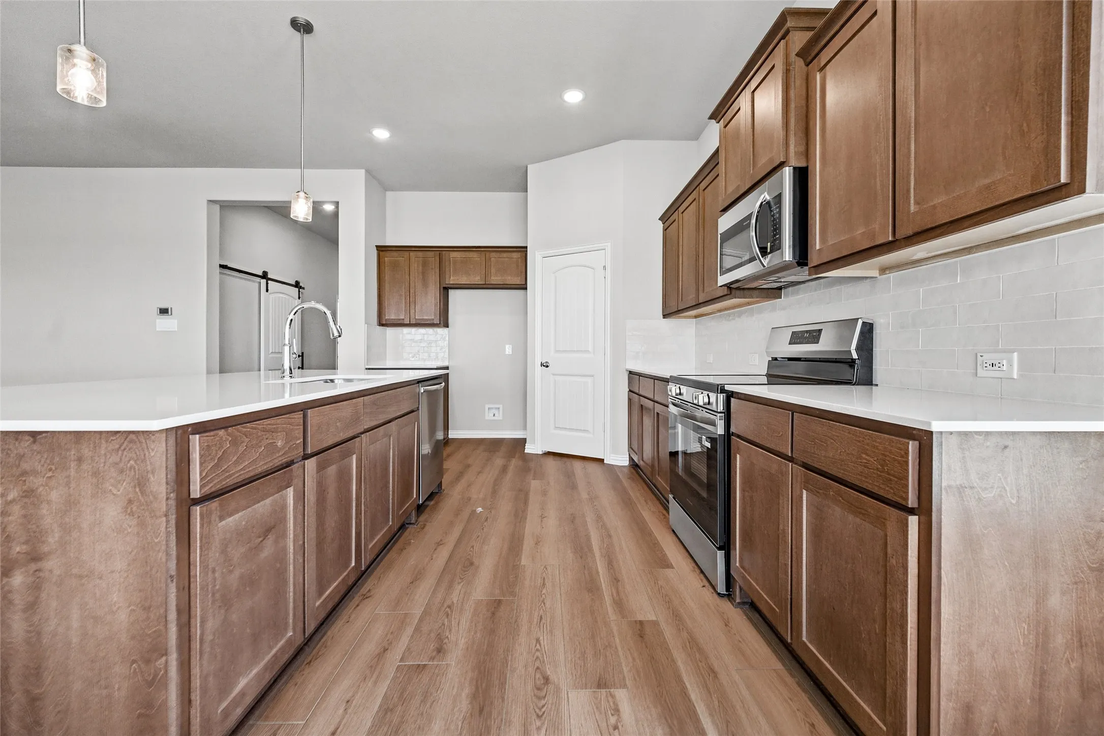 Expansive kitchen featuring wood-finish flooring, shaker-style cabinetry, stainless steel appliances, white countertops, and a subway tile backsplash