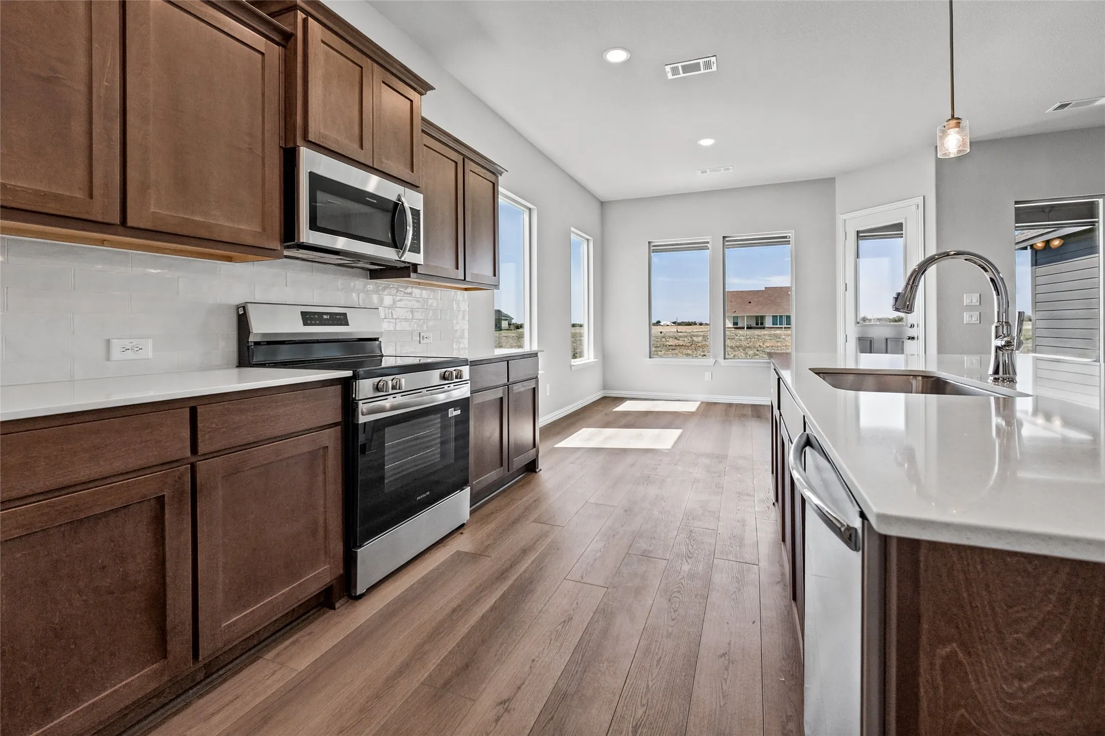 Kitchen featuring wood-finish flooring, stainless steel appliances, solid surface countertops, a subway tile backsplash, and a kitchen island with an undermount sink