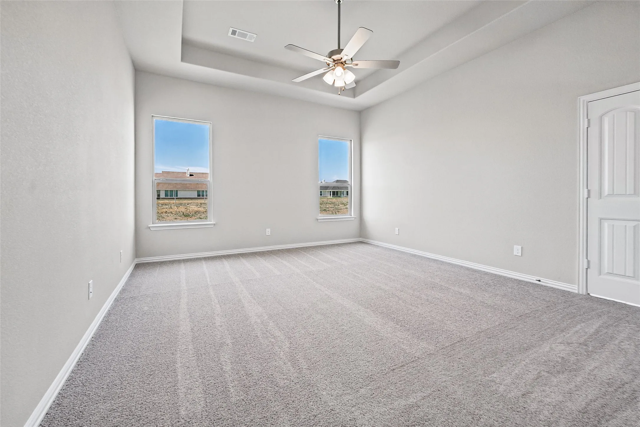 Spacious room featuring a tray ceiling, ceiling fan, two windows, and light gray carpeting