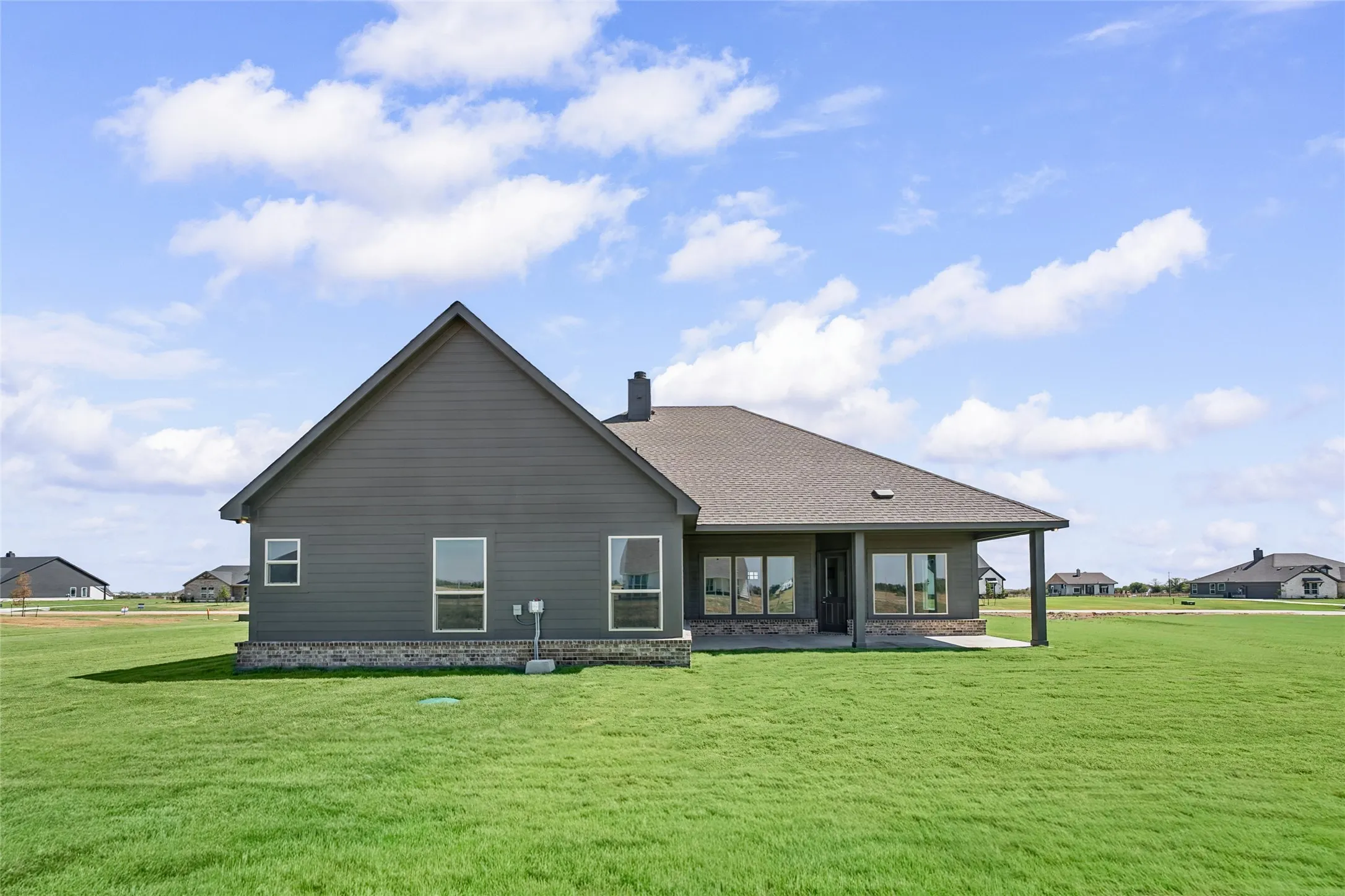 Expansive green lawn bordering the property, with a covered patio featuring dark support pillars