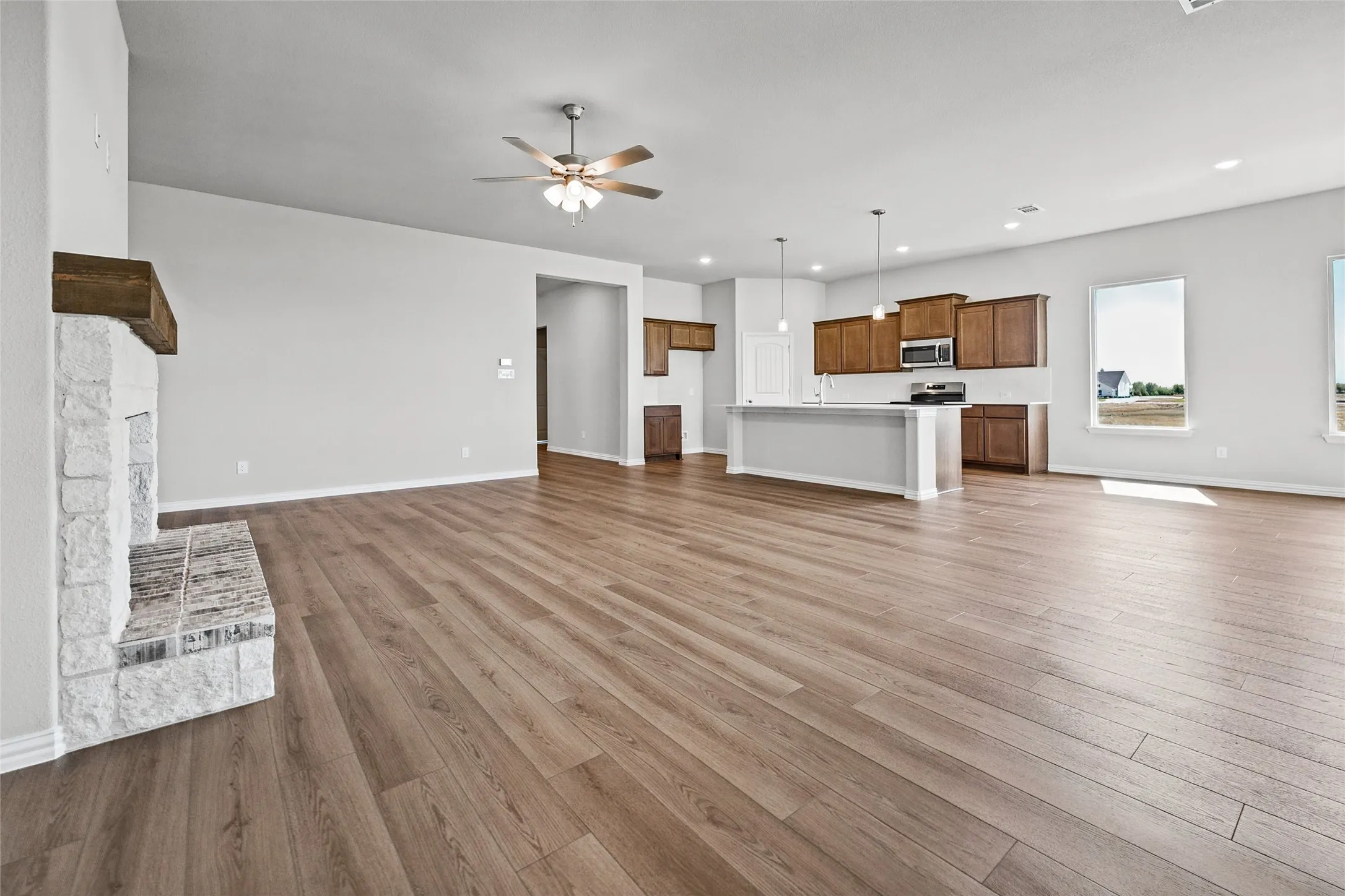 Spacious living area featuring wood-finish flooring, a stone fireplace with a wood mantle, and a ceiling fan