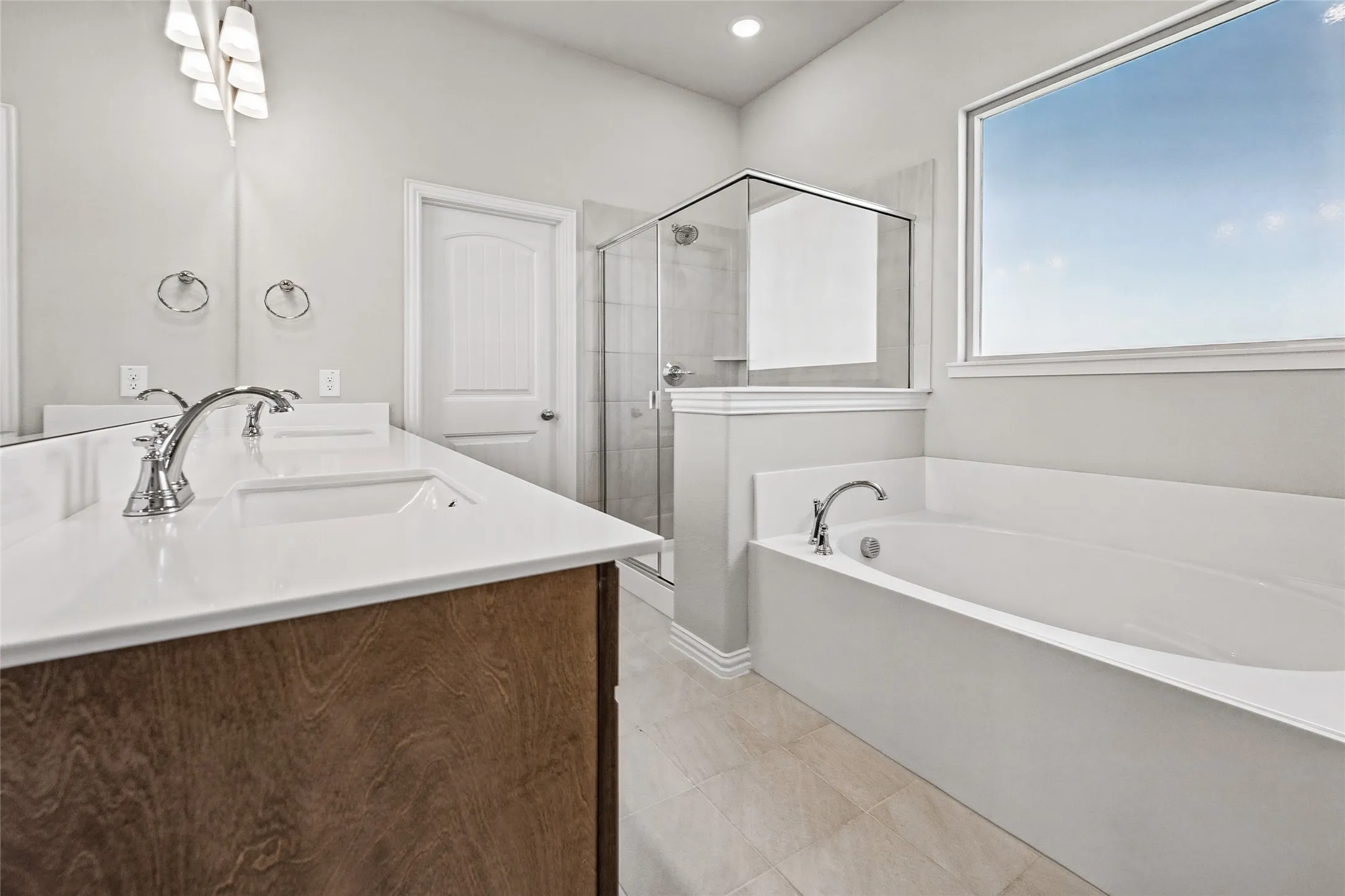 Dual vanity with integrated sinks, wood-finish cabinetry, built-in soaking tub, and a glass-enclosed shower