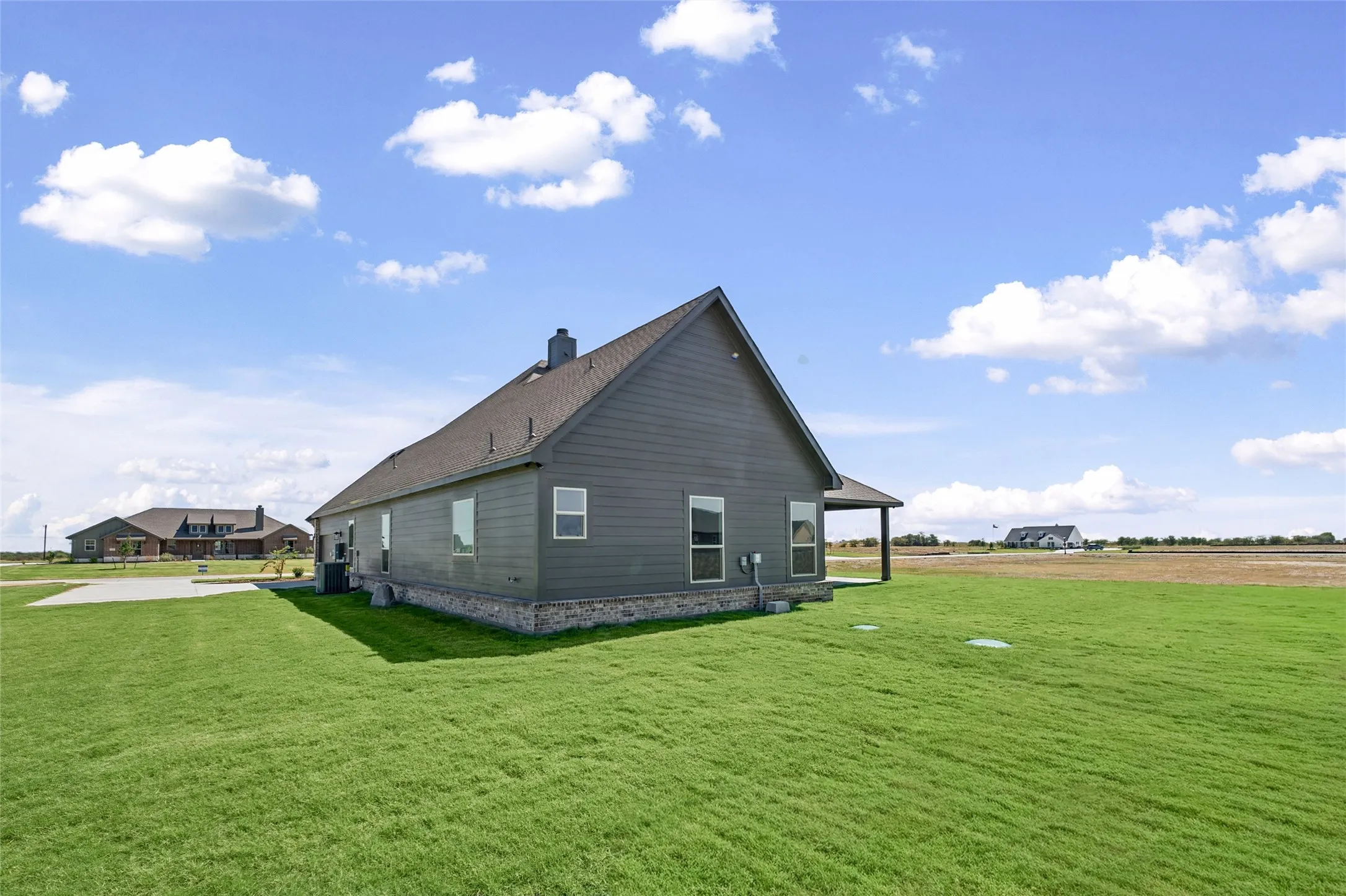 Expansive green lawn surrounds the home, featuring a dark gray exterior, gable roof, and stone-clad foundation