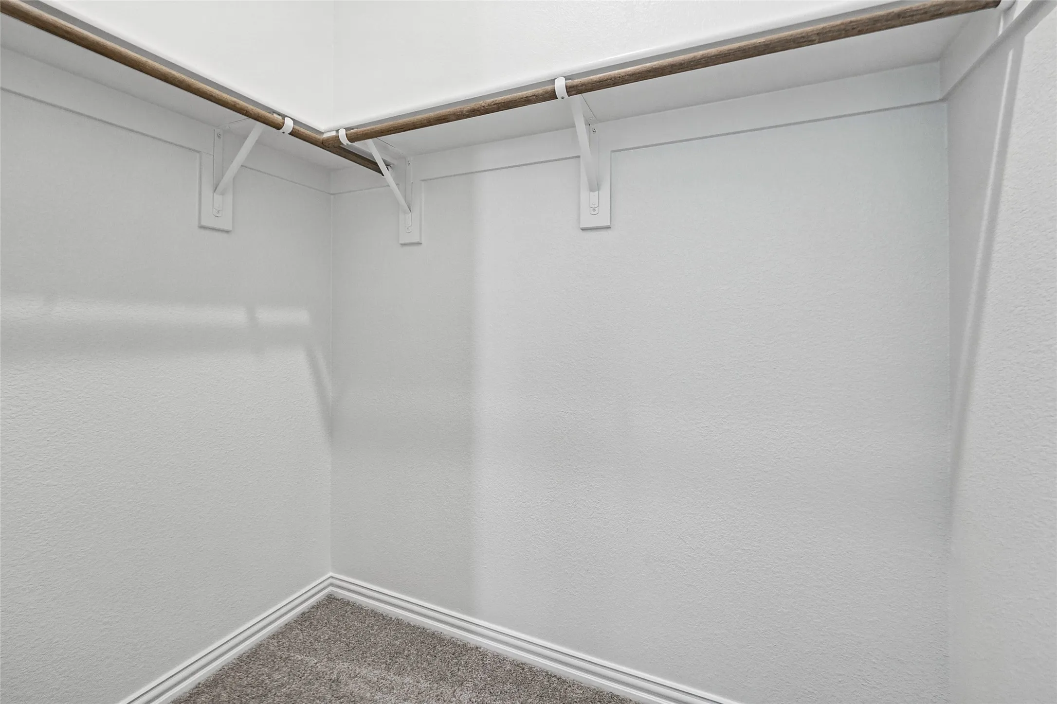 Carpeted closet space with corner-mounted hanging rods and white trim