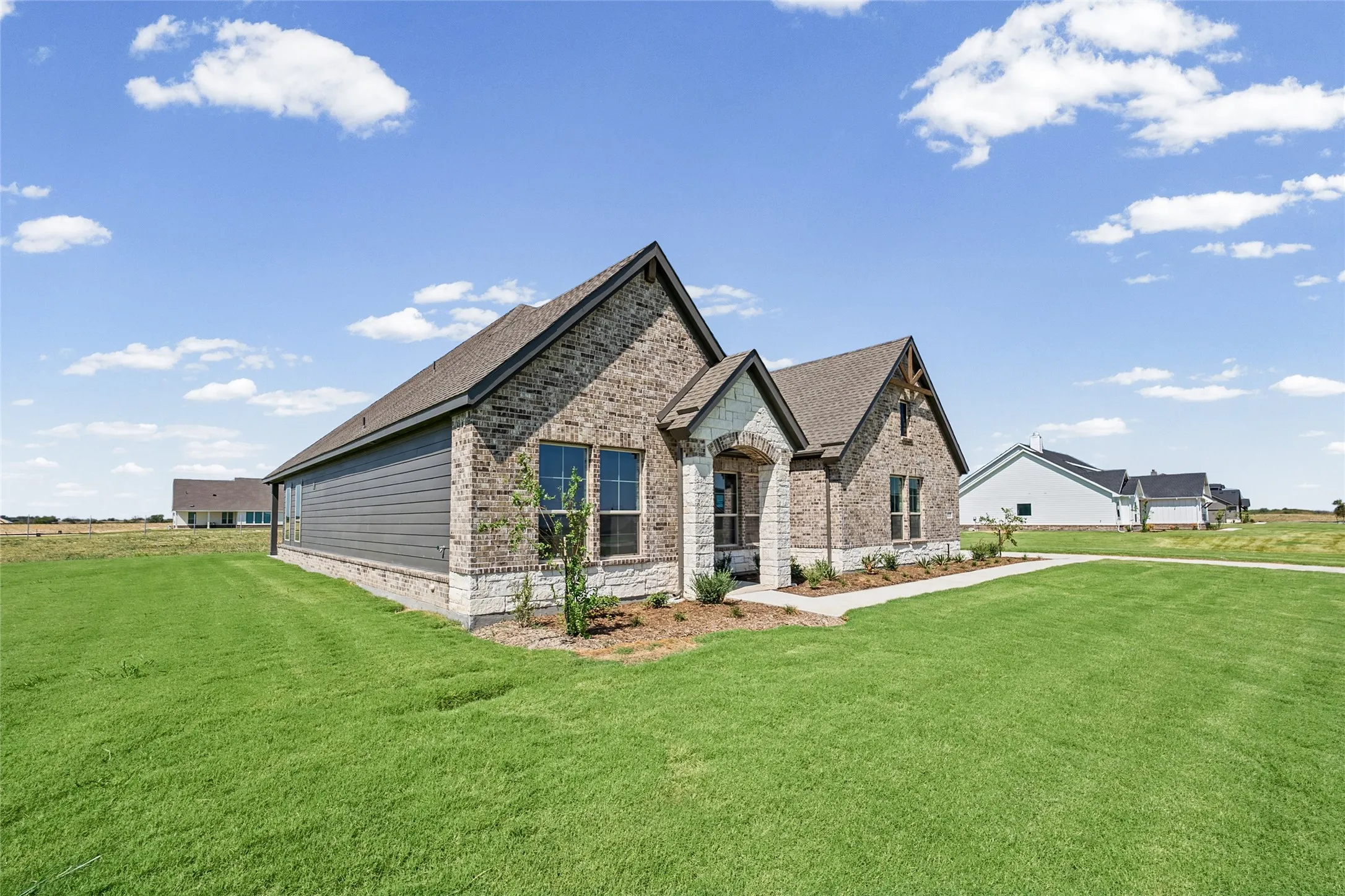 Brick and stone exterior with gray siding accents, gabled roofline, front landscaping, and an inviting entry porch